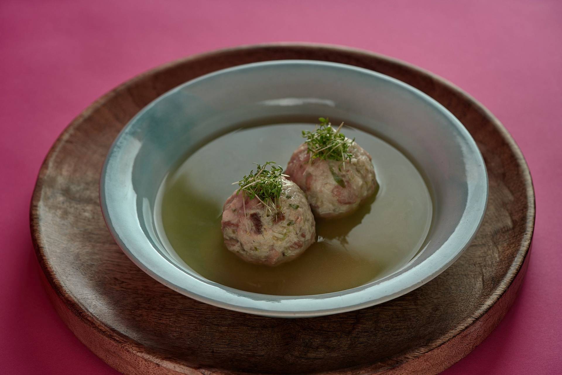 vegan bread dumplings with brussels sprouts and vegetable broth on a turquoise plate with pink background