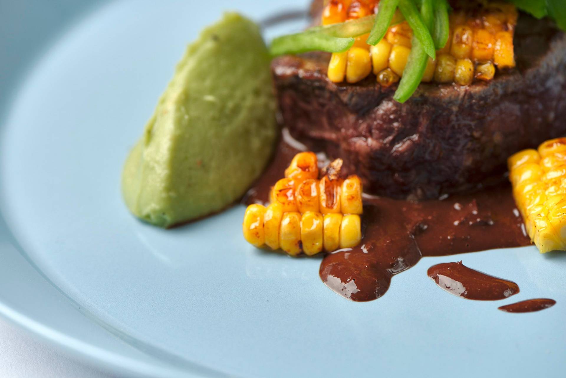 beef steak with dark beer mole sauce corn and guacamole on a blue plate
