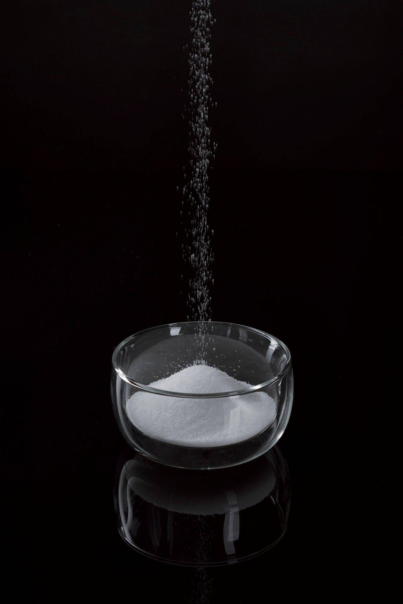 salt and sugar in a glass bowl with black background