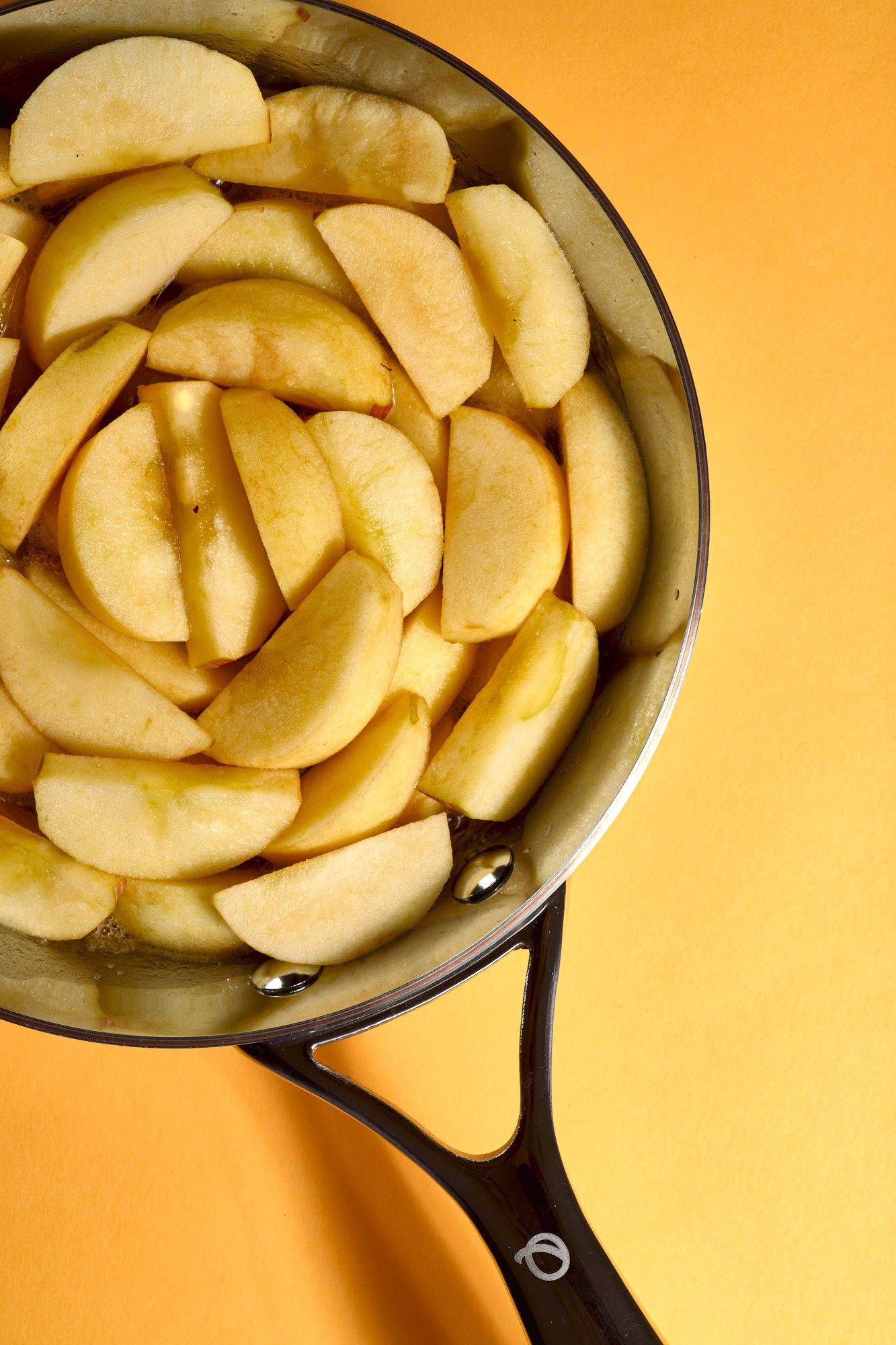 making apple and ginger tarte tatin in a silver olav pan with yellow background