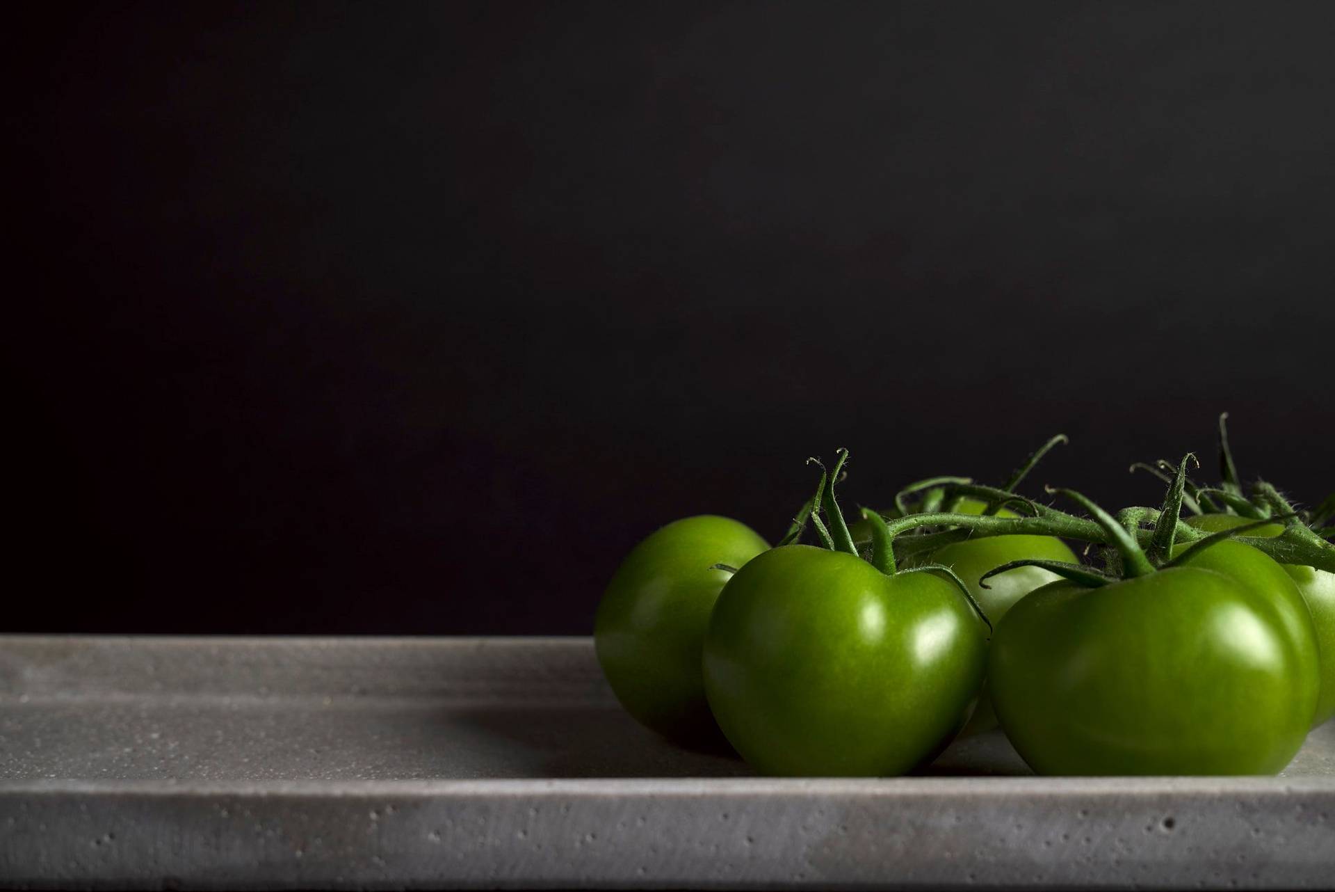 fünf grüne tomaten auf einer betonplatte auf schwarzem hintergrund