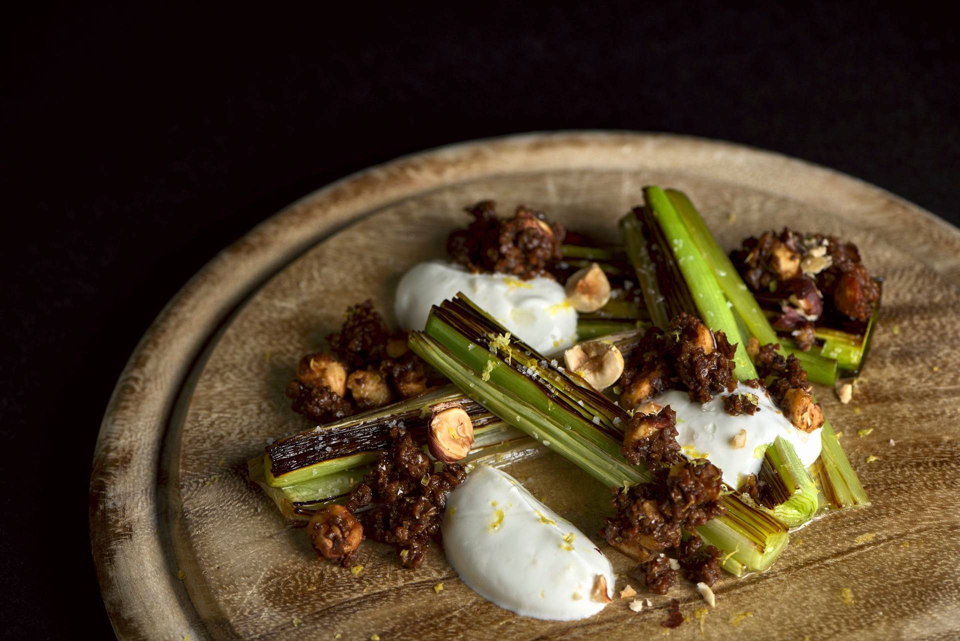 beer braised leek with pumpernickel and skyr on a wooden board with black background