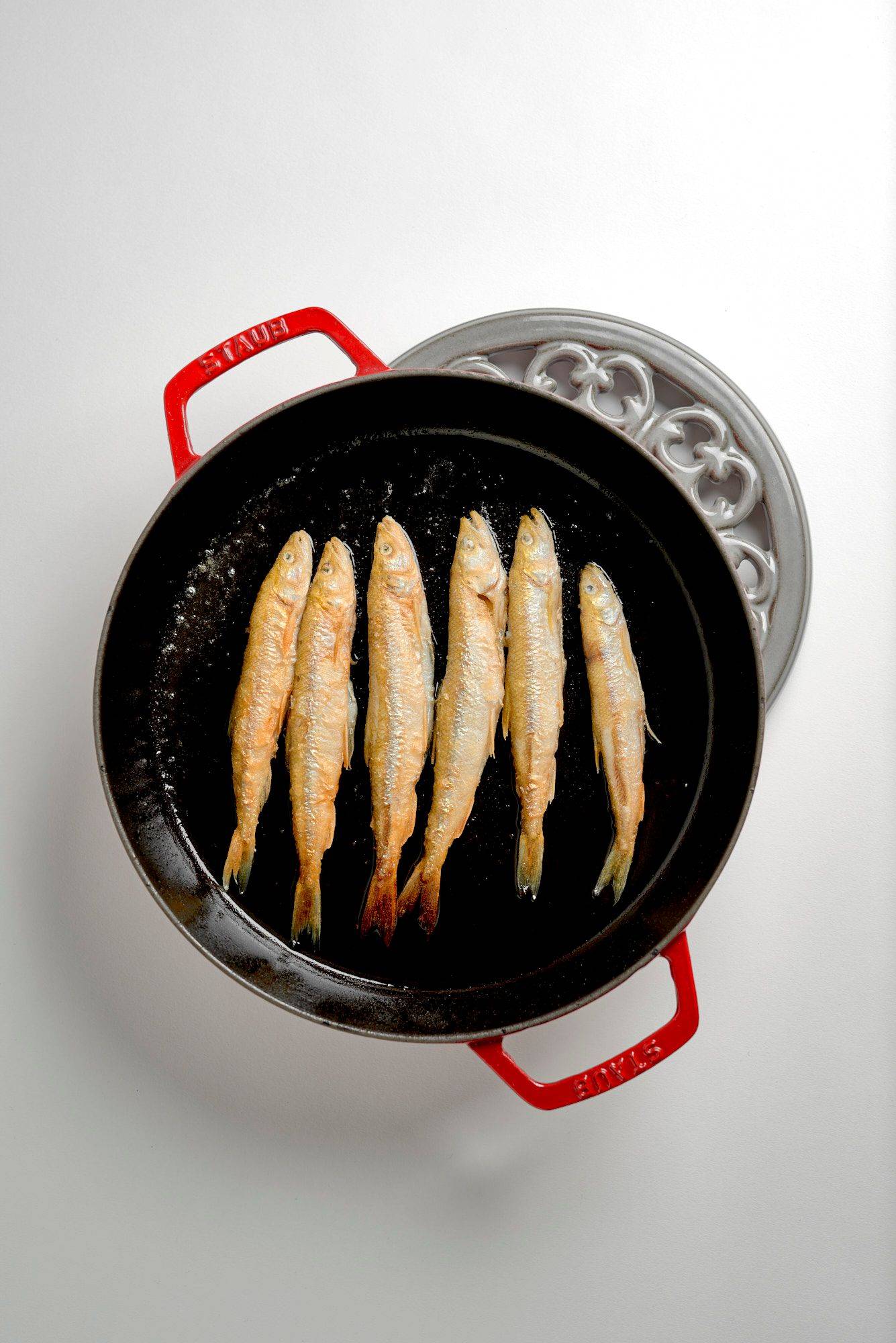 fried crispy smelt fish in a red staub cast iron pan on white background