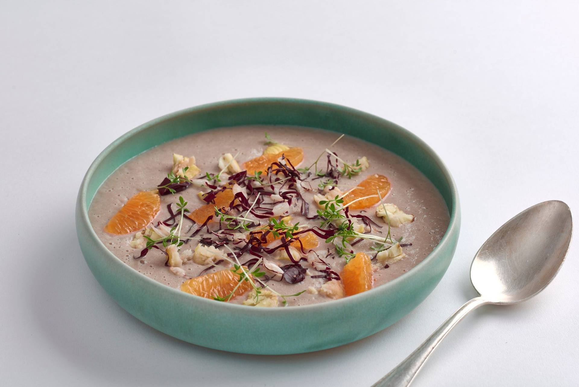 parsnip soup with radicchio tangerine and chestnuts in a turquoise bowl on white background