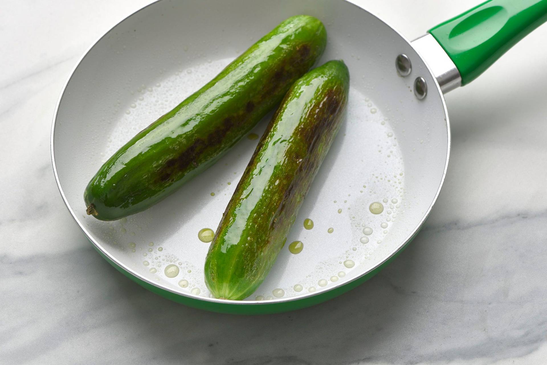 two charred cucumbers in a green pan with a marbled sapienstone top