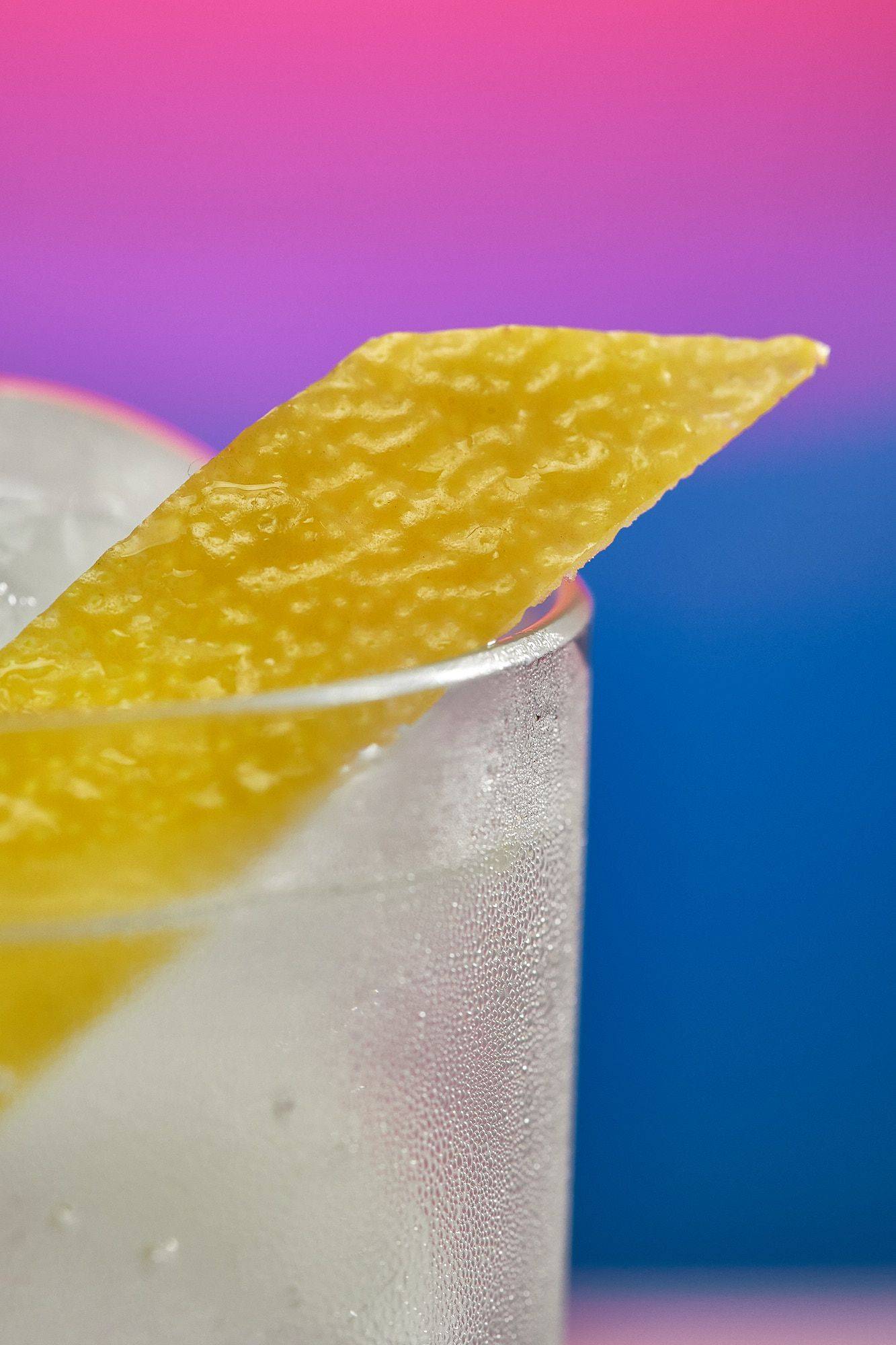 a glass of spicy ginger lemon mocktail on rainbow colored background
