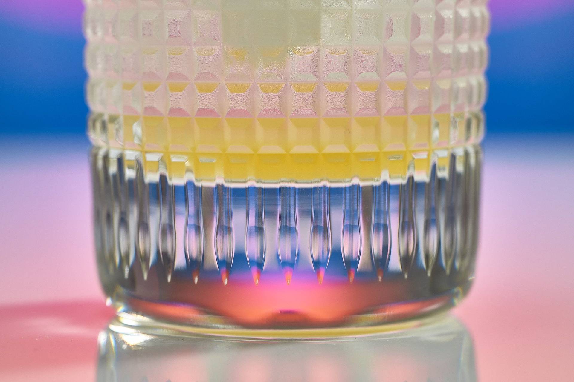 ein glas mit alkoholfreiem ingwer-zitronen cocktail vor regenbogenfarben hintergrund