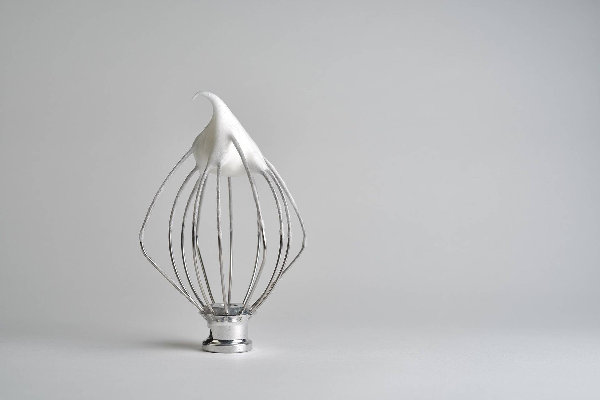 a whisk with meringue on white background