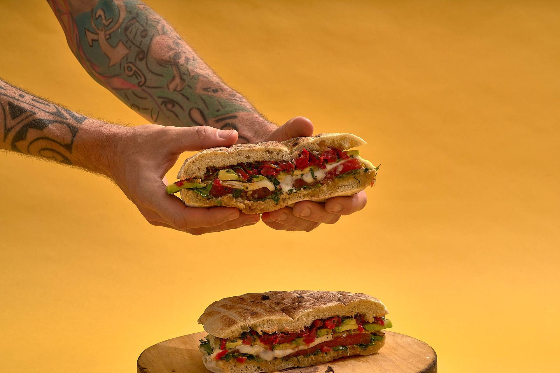 hände halten vegetarisches sandwich mit gegrillter wassermelone gremolata knoblauchpaste und käse auf holzbrett mit gelbem hintergrund