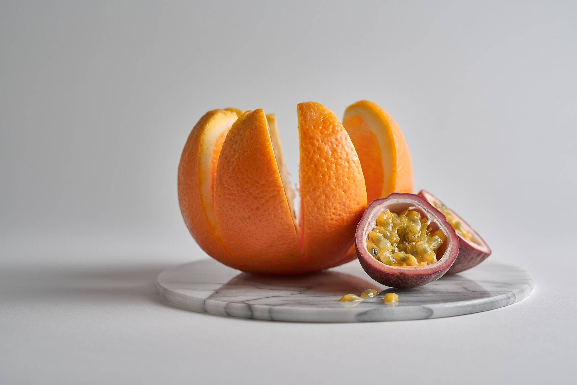 eine Orange und Passionsfrucht auf einem Marmorteller vor weißem Hintergrund