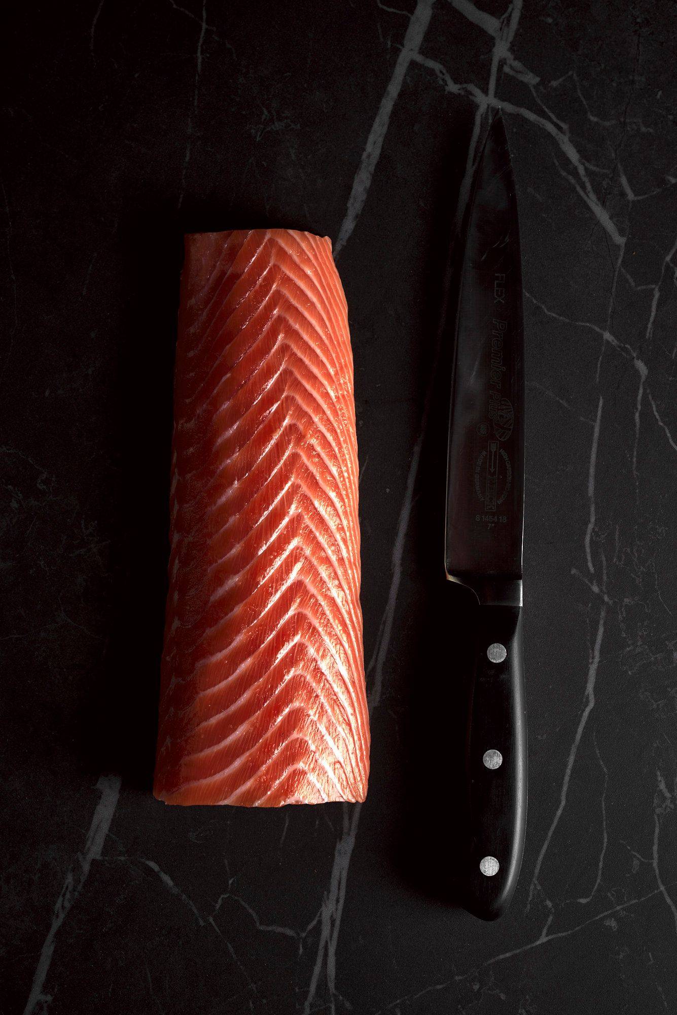a raw salmon loin with a kitchen knife on a gray sapienstone top