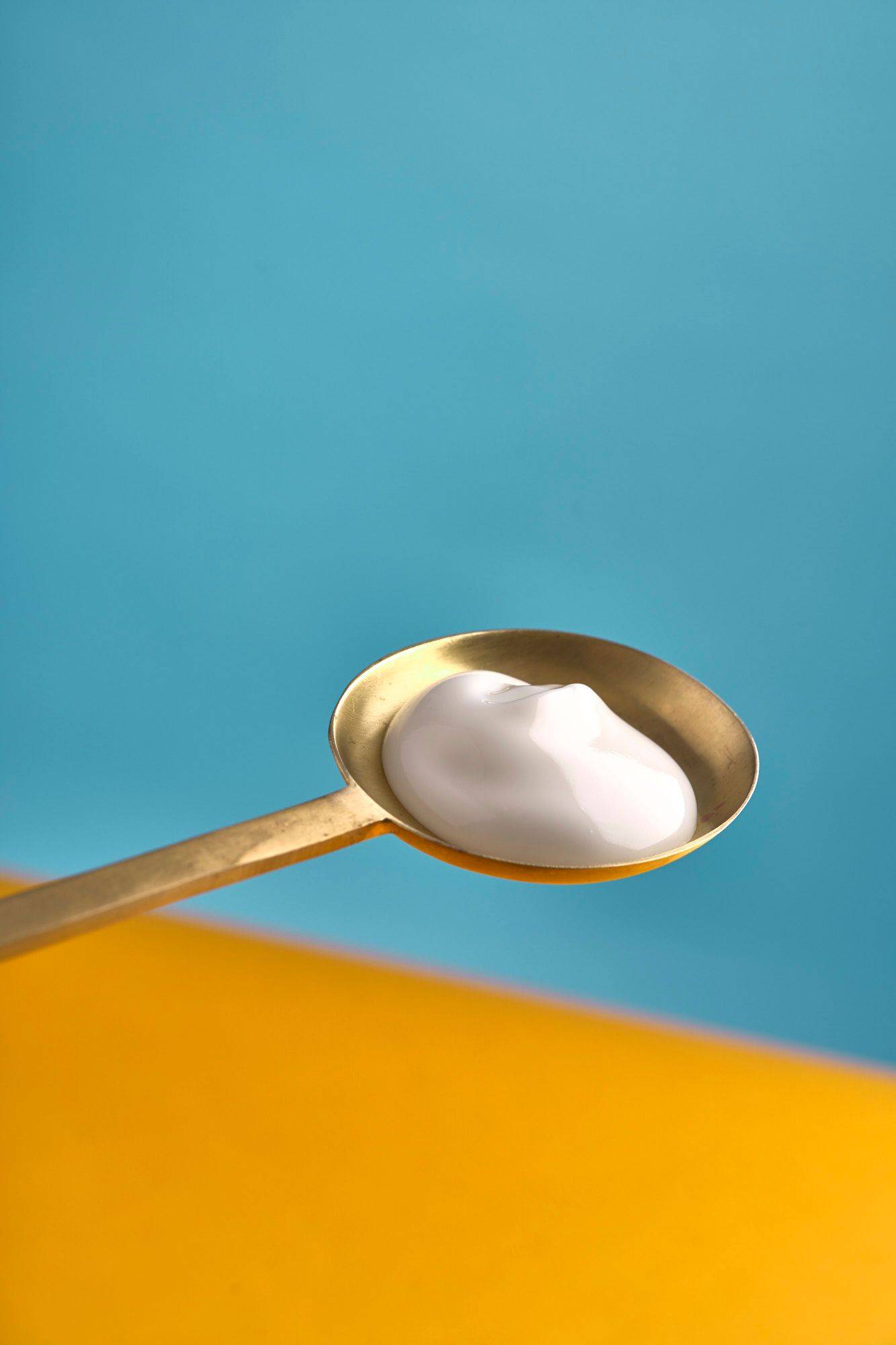 greek yogurt on a brass spoon with yellow and blue background