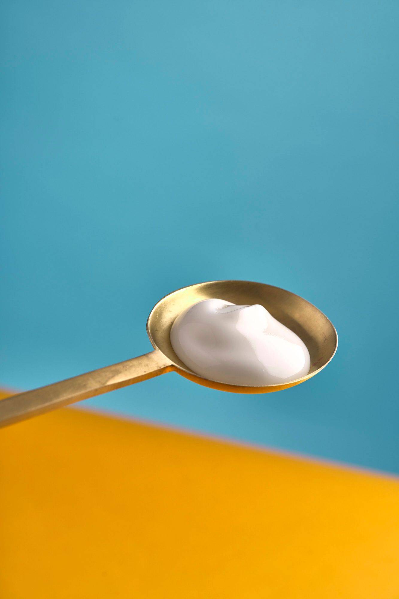 greek-yogurt greek yogurt on a brass spoon with yellow and blue background