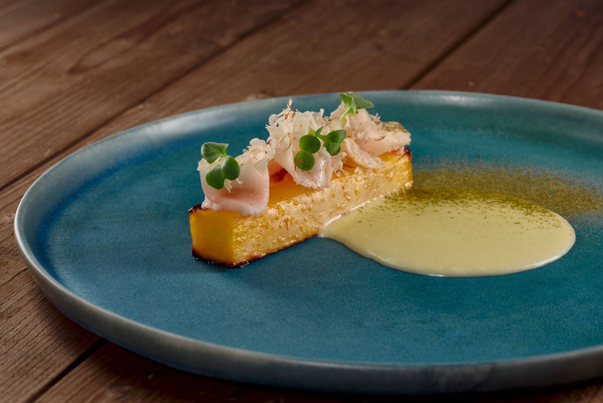 steckrübe mit lardo speck und salzgurken beurre blanc auf einem blauen teller mit holztisch 