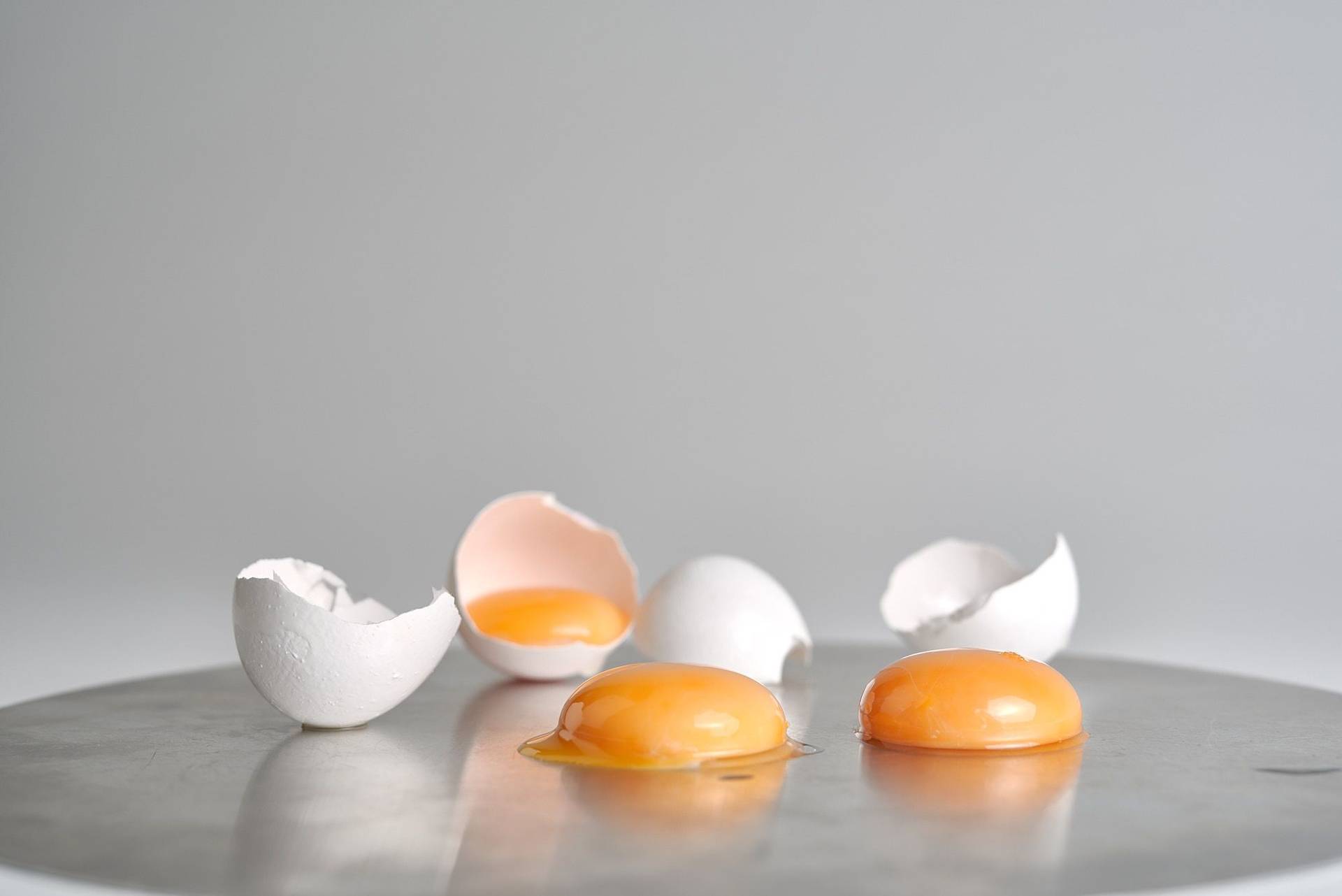 three egg yolks with egg shells on a cake plate with white background