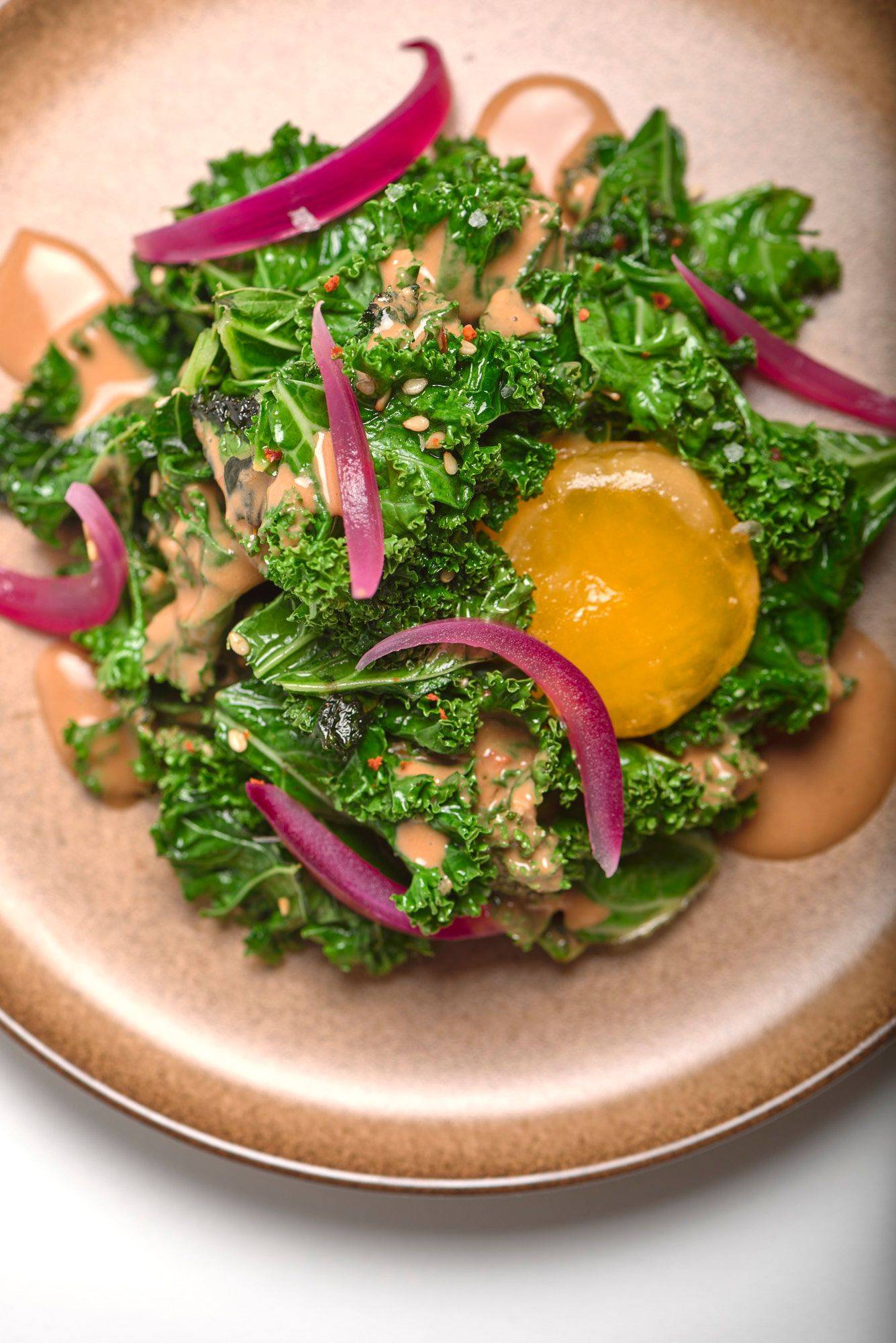 grünkohl salat mit miso eigelb und hagebutte auf einem braunen keramik teller mit weißem hintergrund