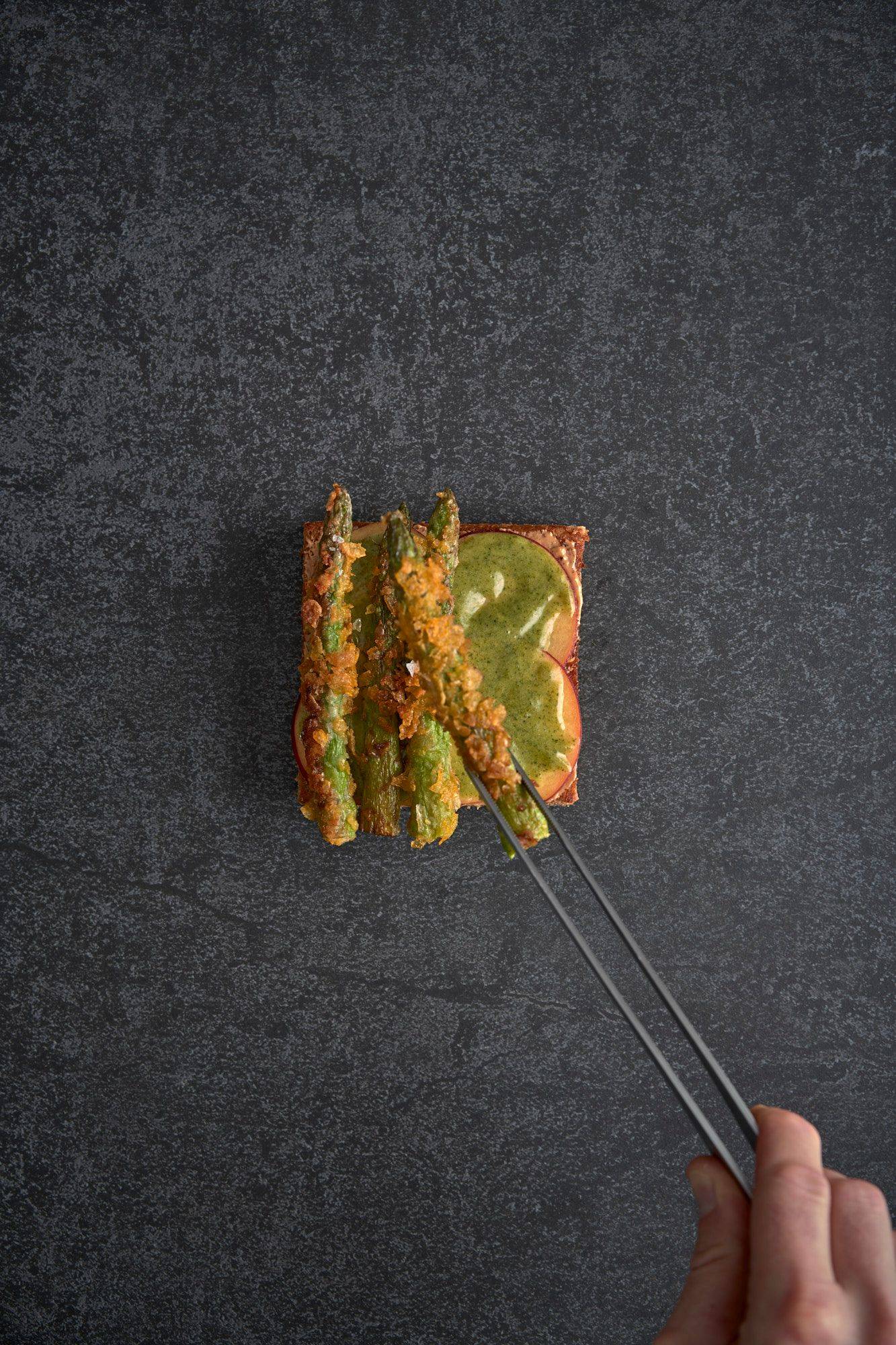 assembling a vegetarian asparagus katsu sando with nectarine and mint mayonnaise on a gray sapienstone top