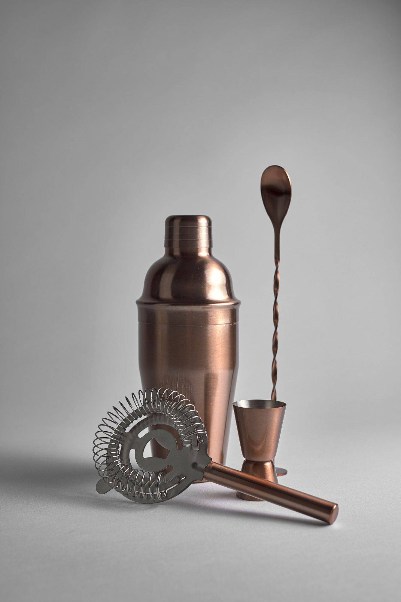 cocktail-tools a copper jigger, spoon, strainer and measuring cup on white background