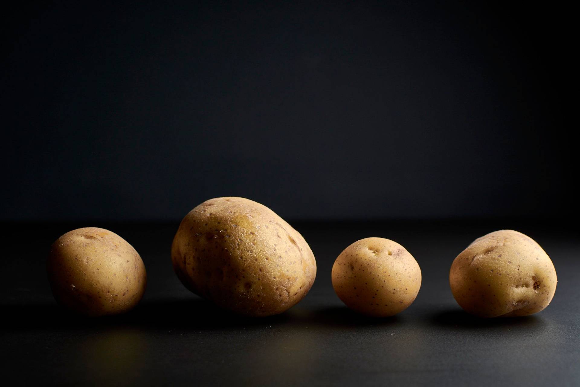 vier kartoffeln in einer reihe auf schwarzem hintergrund