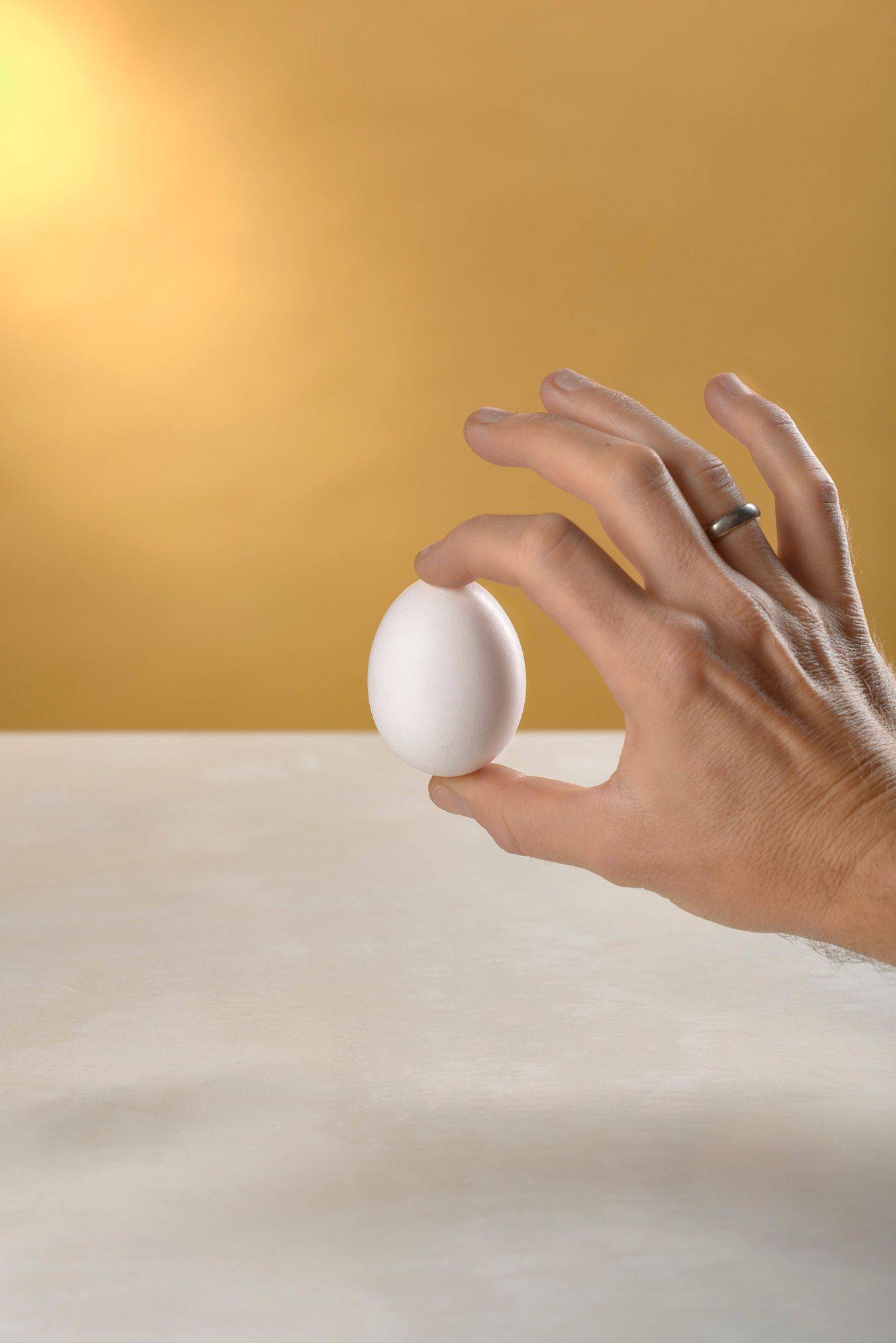 hand holding a white egg on white sapienstone top with yellow background