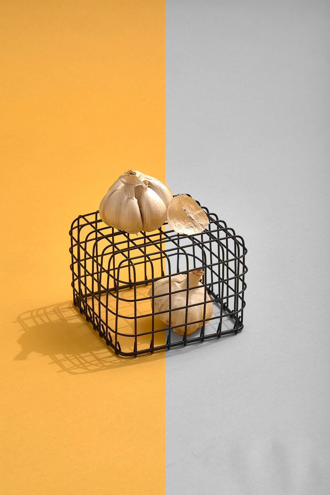 garlic in black metal basket on yellow background