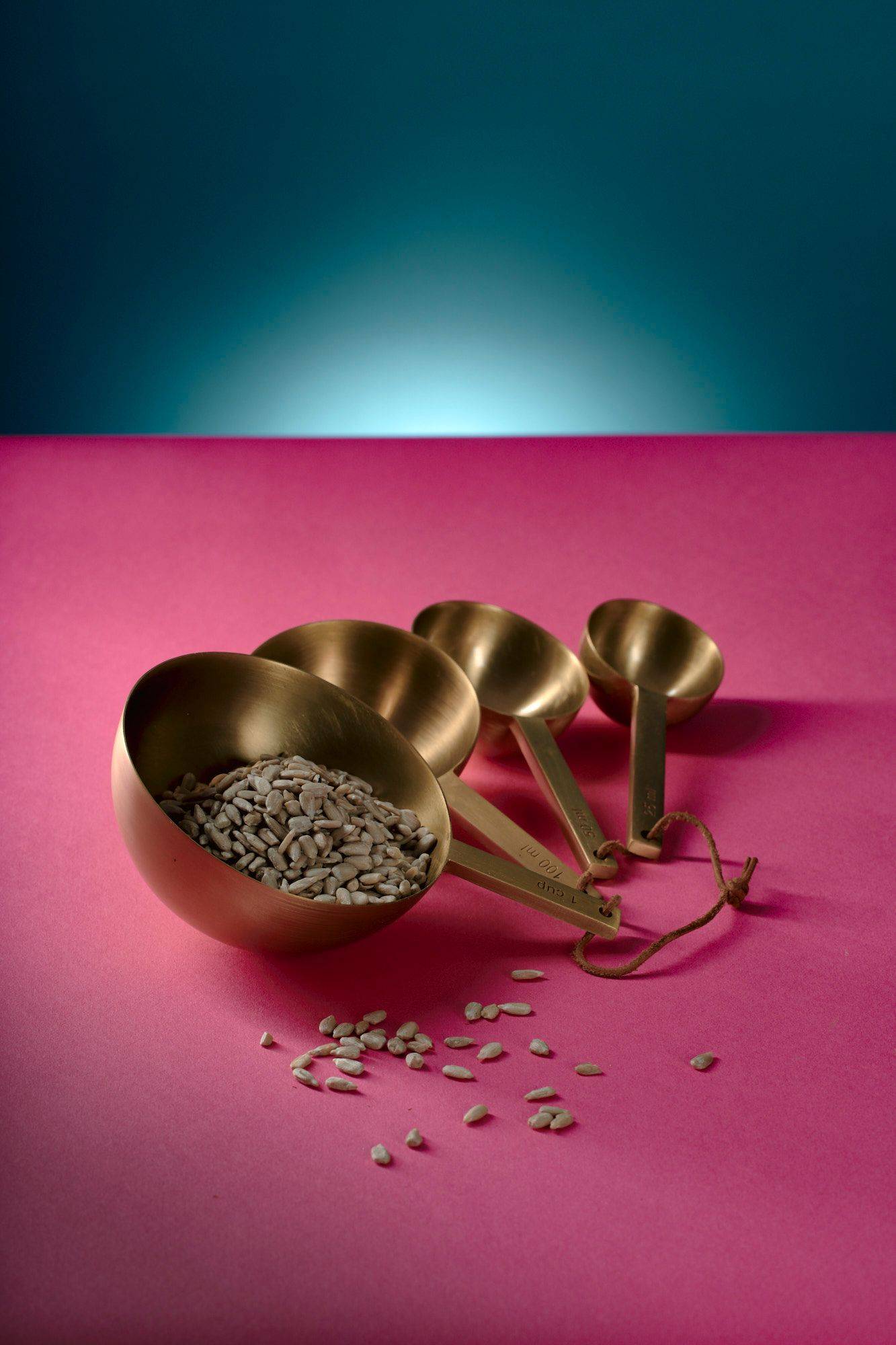 sunflower seeds in brass measuring spoons with pink and blue background