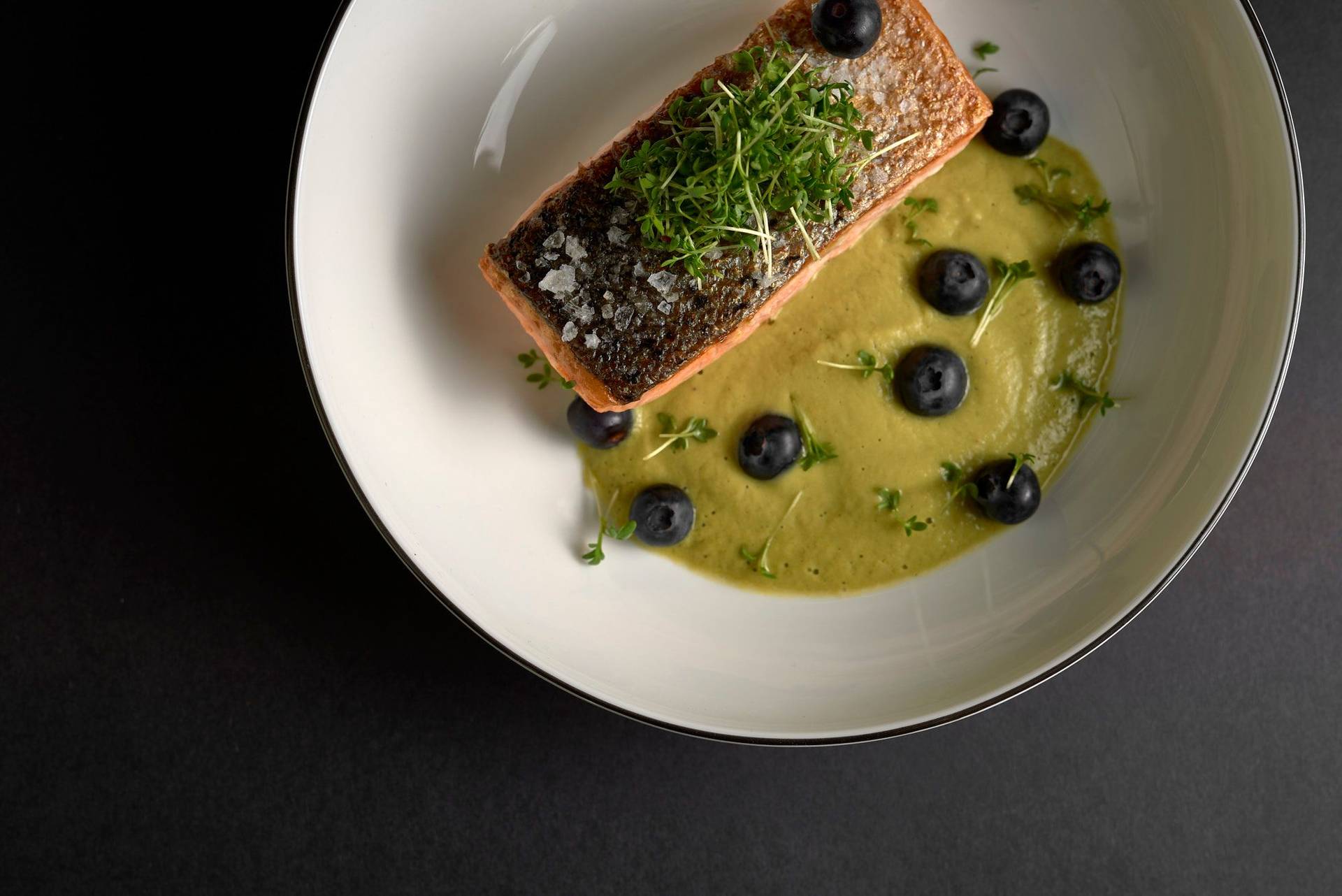 gebratener lachs mit spargel matcha sauce und blaubeeren in einem weißen teller auf schwarzem hintergrund