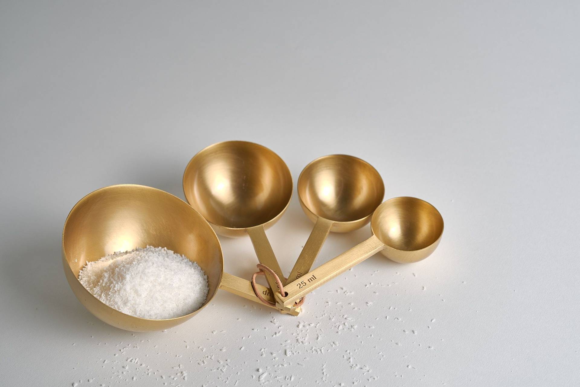 ground coconut in brass measuring spoons on white background
