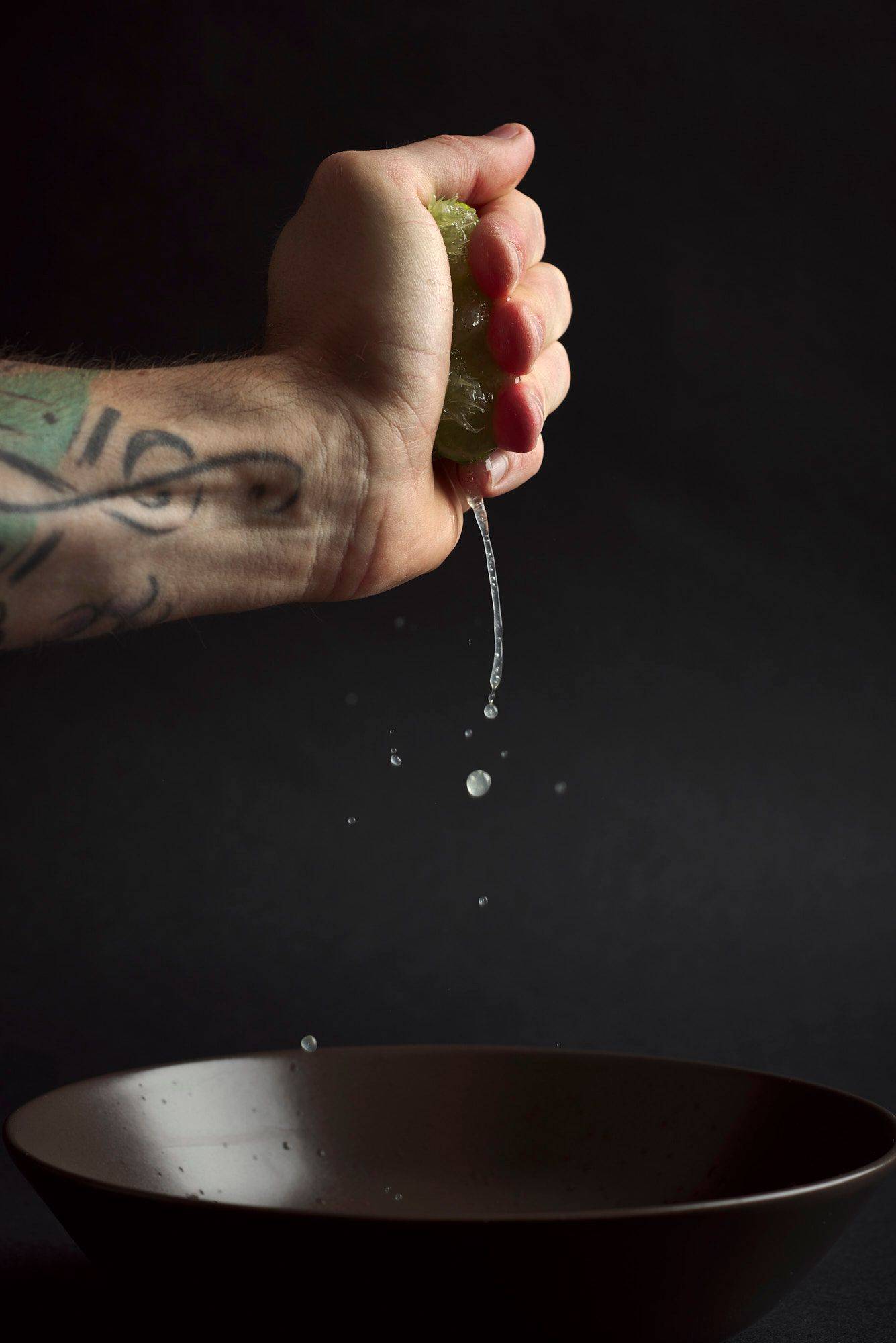 lime-juice hand squeezing lime juicecod ceviche with gooseberries in a turquoise ceramic bowl with black background