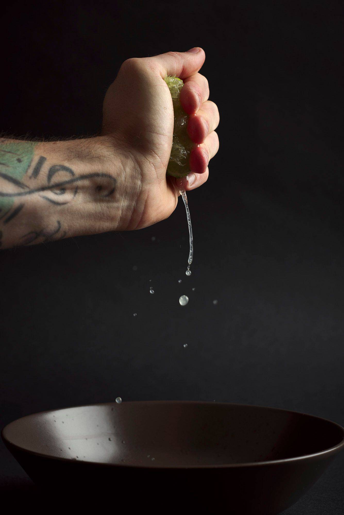 hand squeezing lime juicecod ceviche with gooseberries in a turquoise ceramic bowl with black background