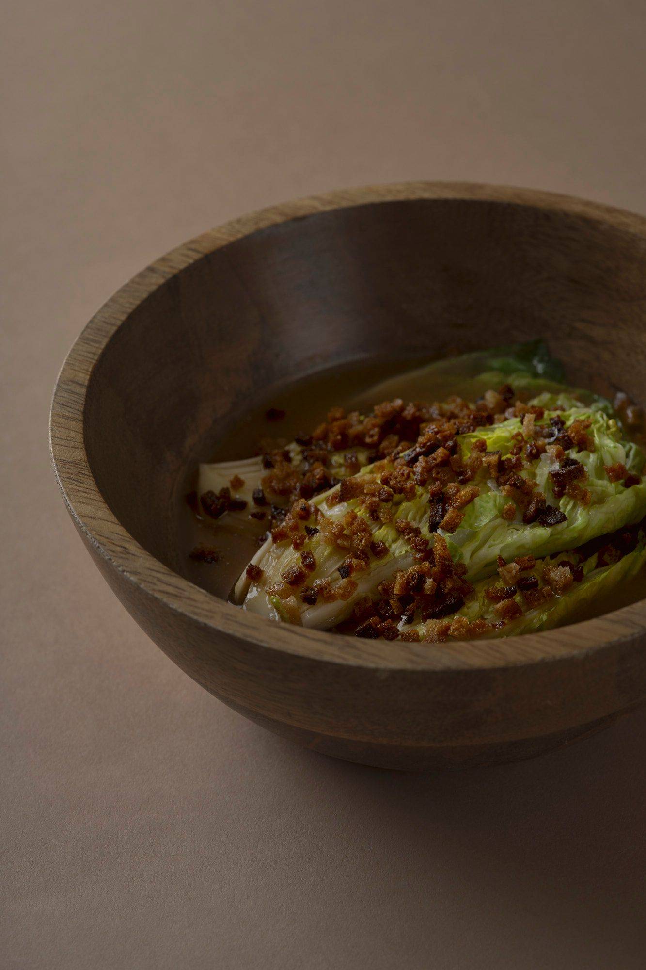 römersalat mit miso sud und sauerteig in einer holzschale mit braunem hintergrund