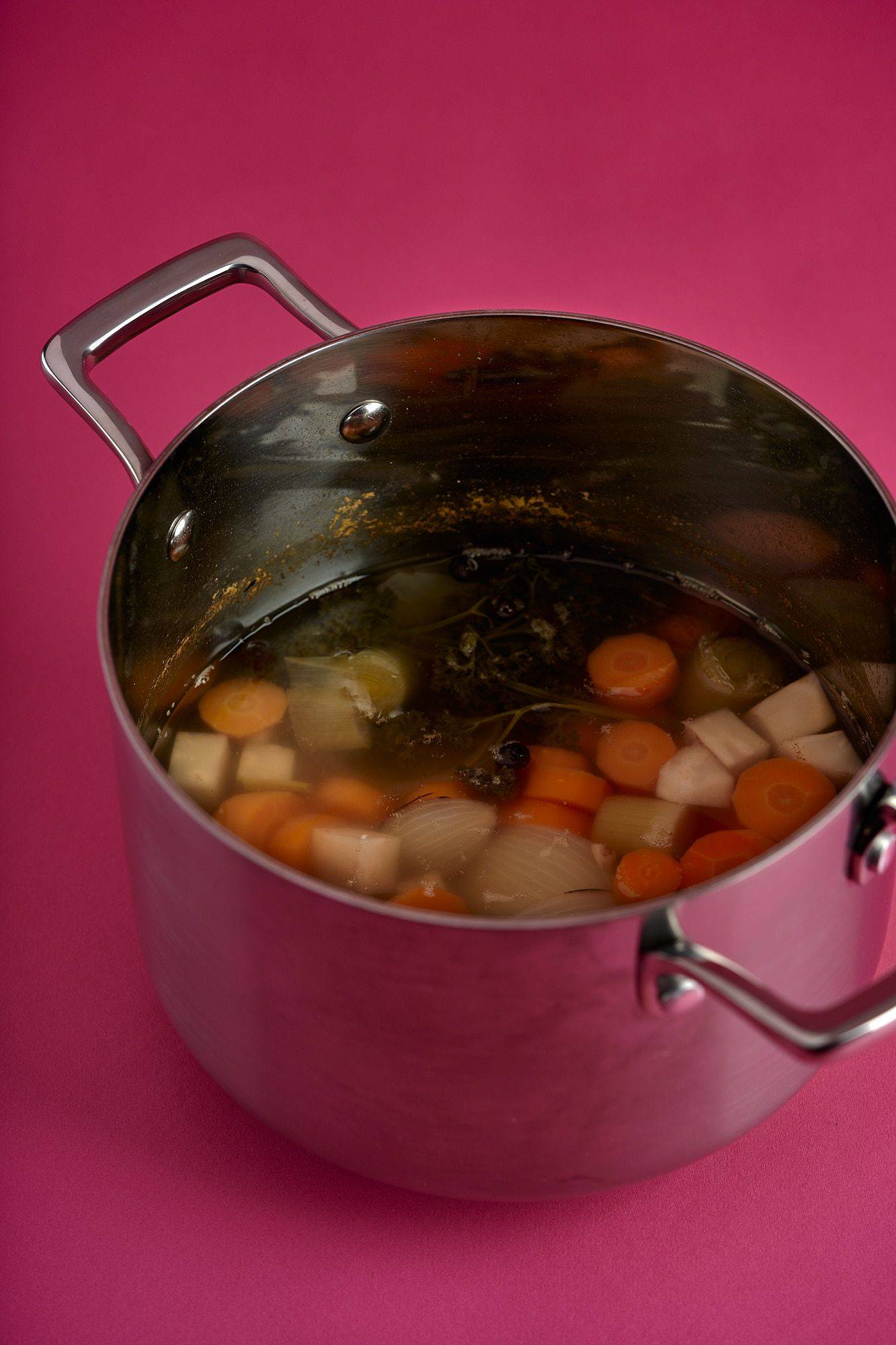 a silver pot with vegetable broth on pink background