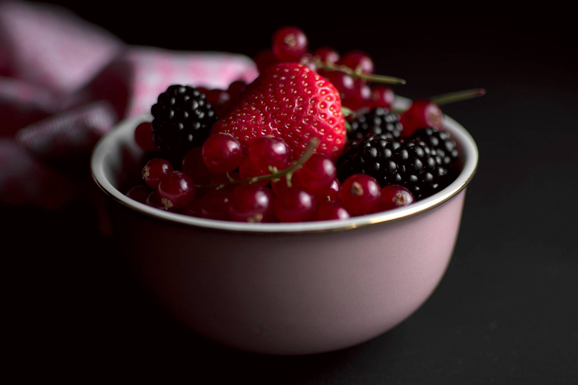 a pink bowl of mixed berries with black background