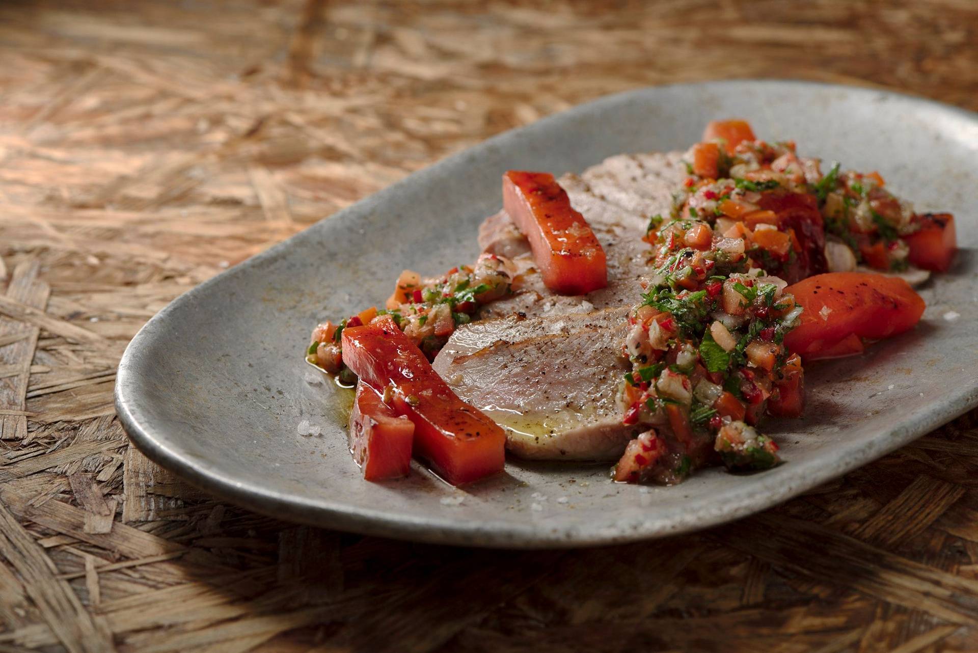 pork secreto with grilled watermelon and chimichurri on a vintage aluminum plate with wooden background