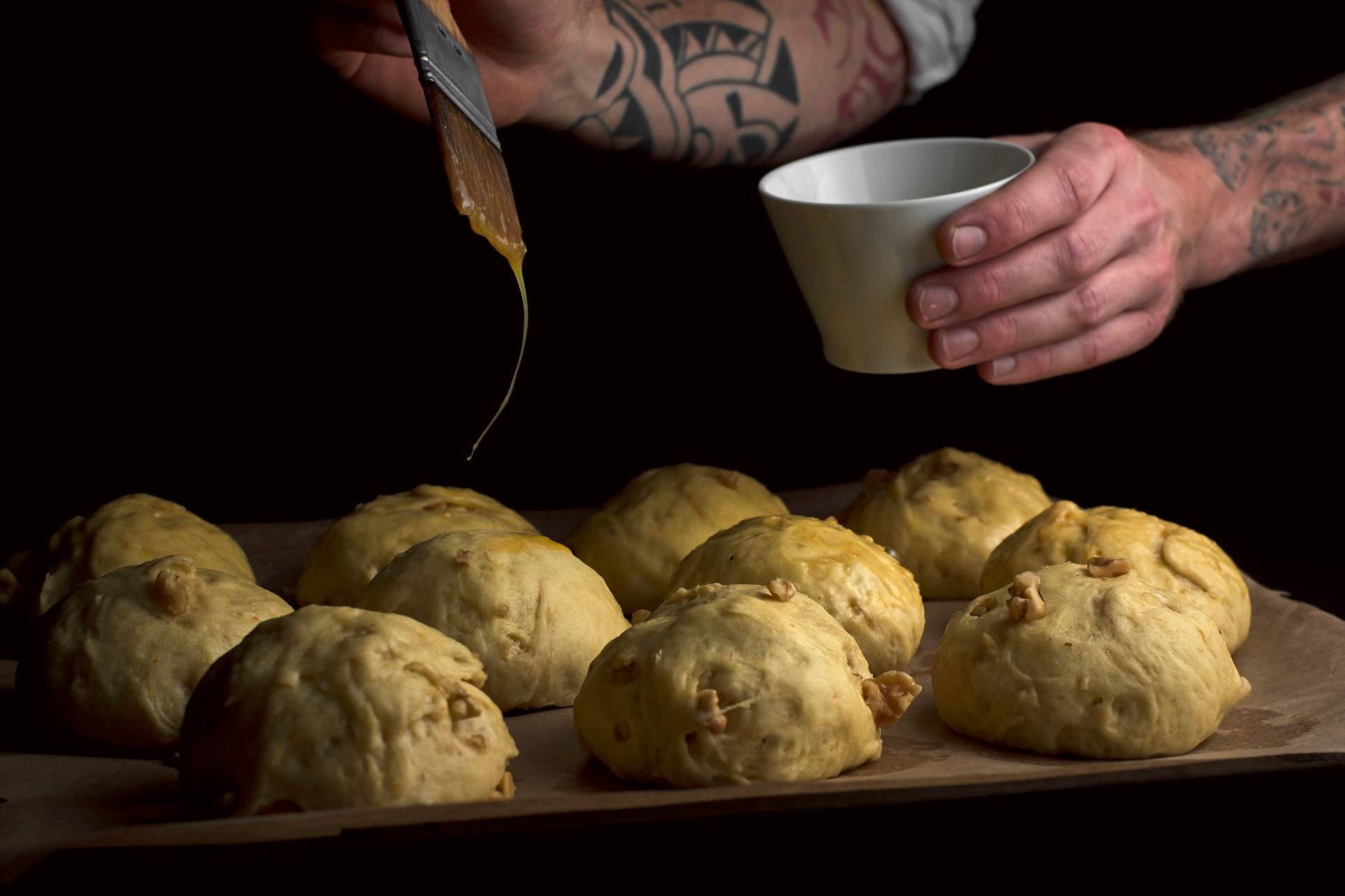 hand bestreicht brioche brötchen mit walnüssen mit ei auf einem backblech mit schwarzem hintergrund