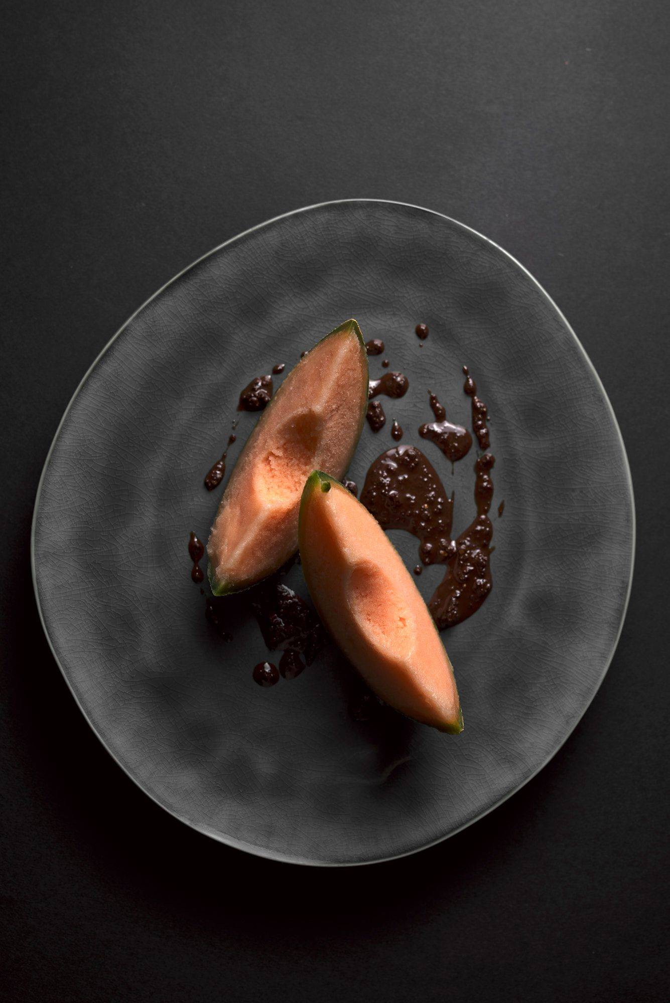 cantaloupe melonen sorbet mit schokoladen pesto auf einem grauen teller mit schwarzem hintergrund