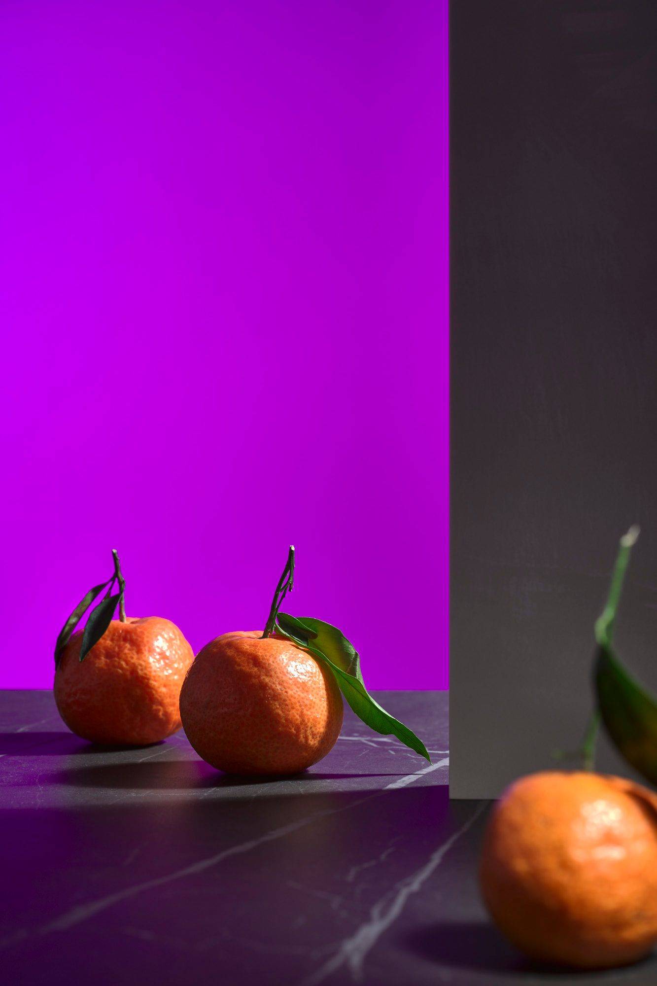 three tangerines with green on a gray marbled sapienstone top with purple background