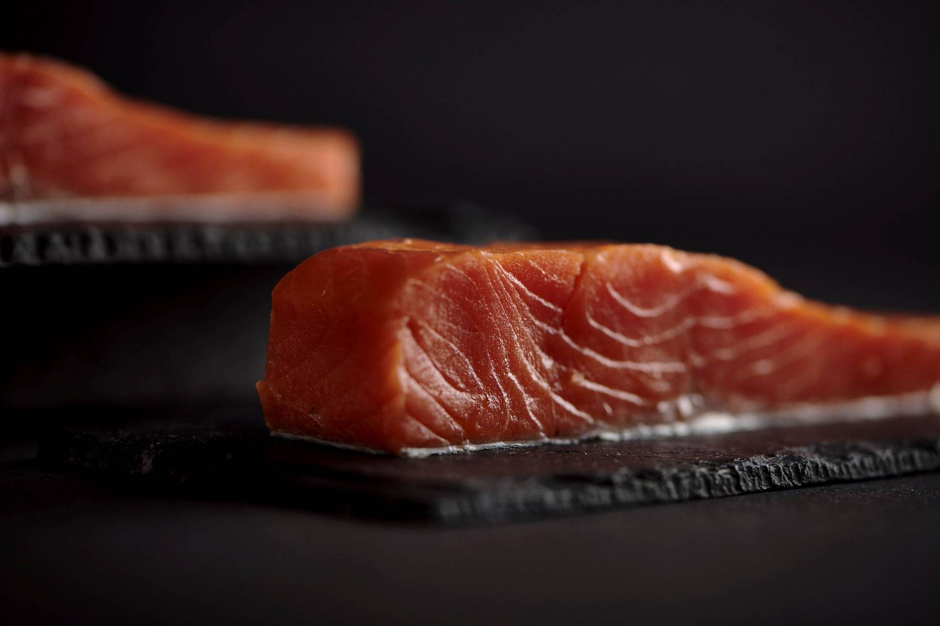 two pieces of cured salmon with black background