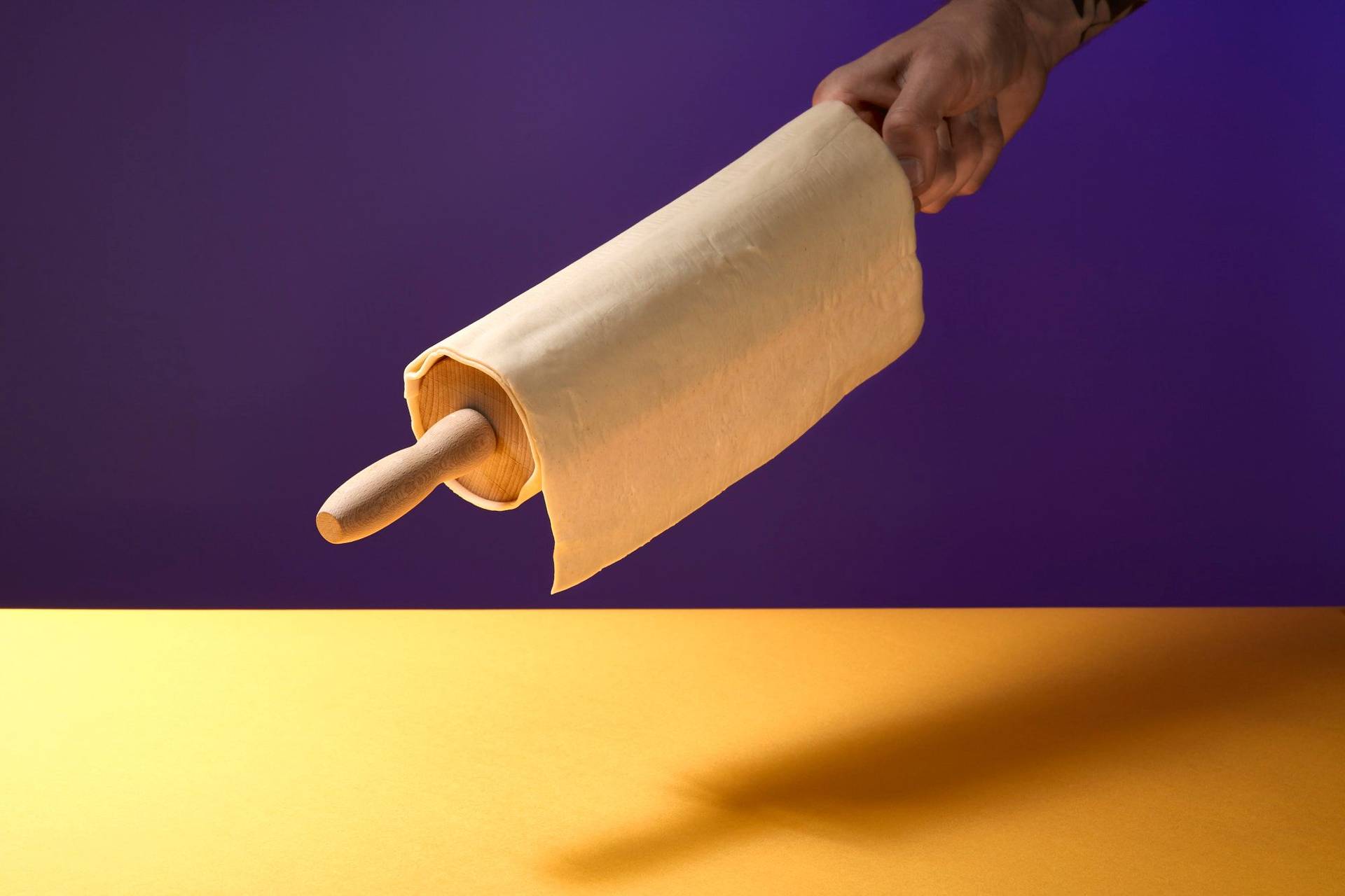 hand hält blätterteig auf einem rollholz mit gelbem und lila hintergrund