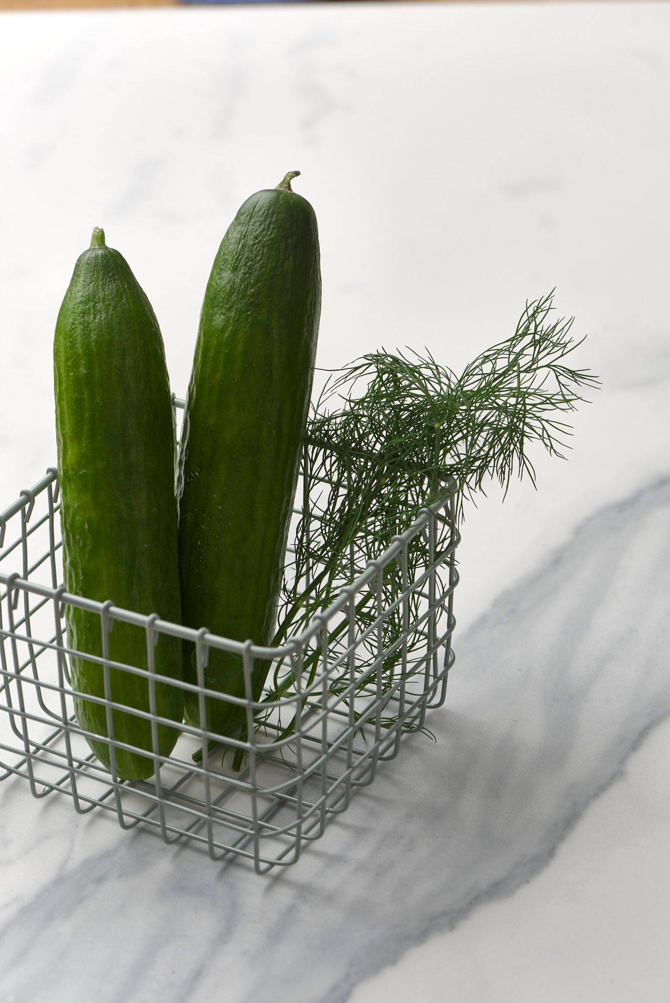 two cucumbers and dill in a small basket with a marbled sapienstone top