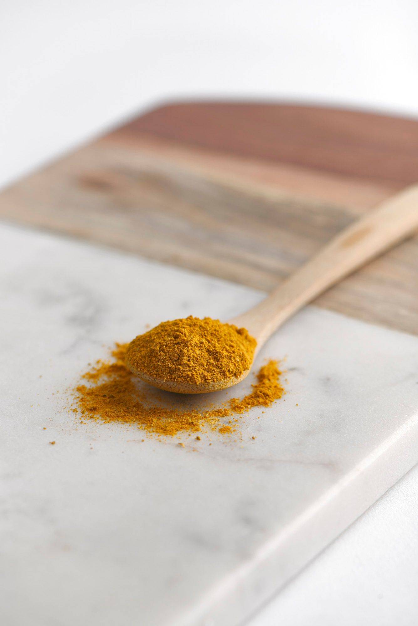 madras curry powder on a wooden spoon on a gray plate with white background