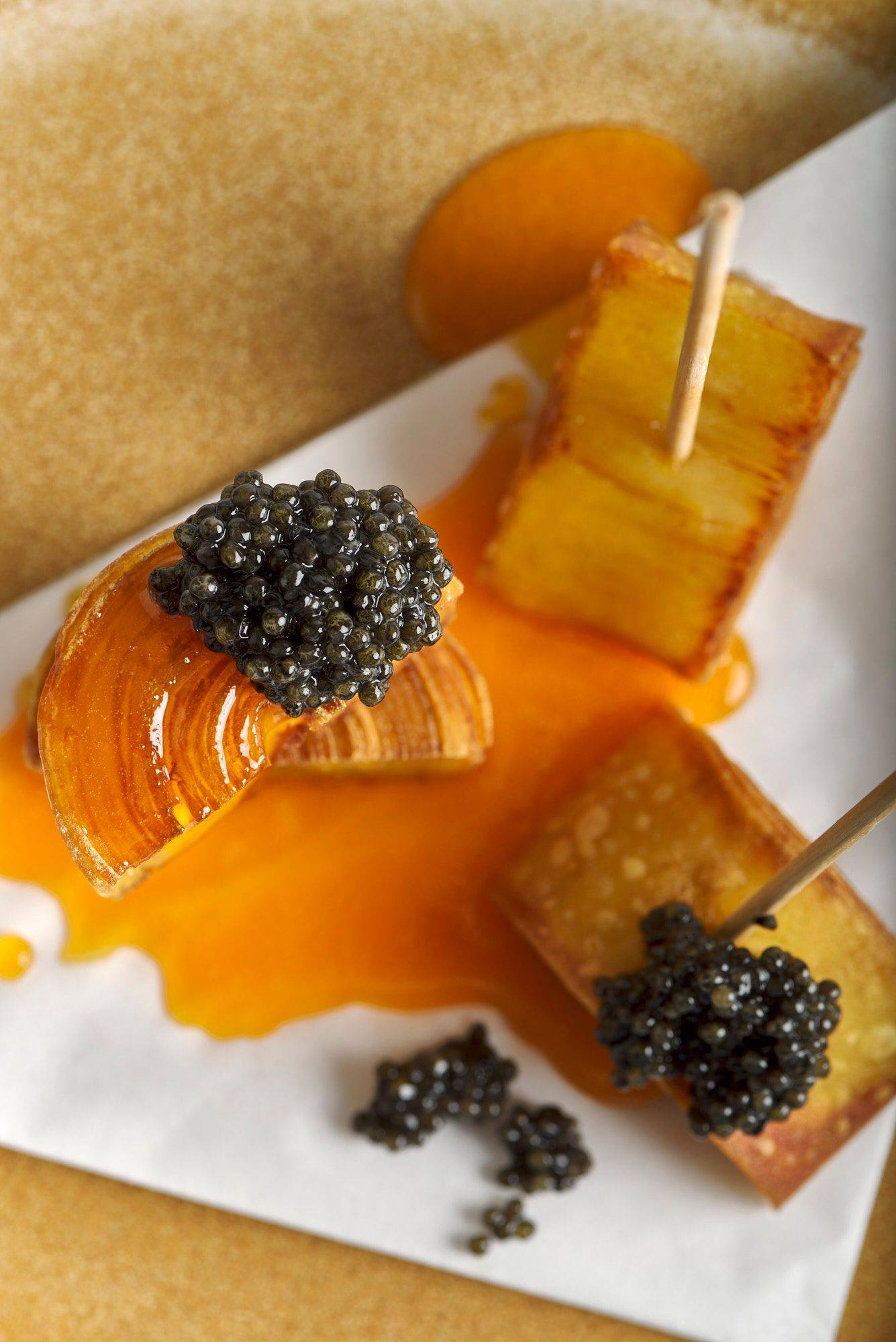 crispy potato swirls with egg yolk and caviar on a brown ceramic plate with white background