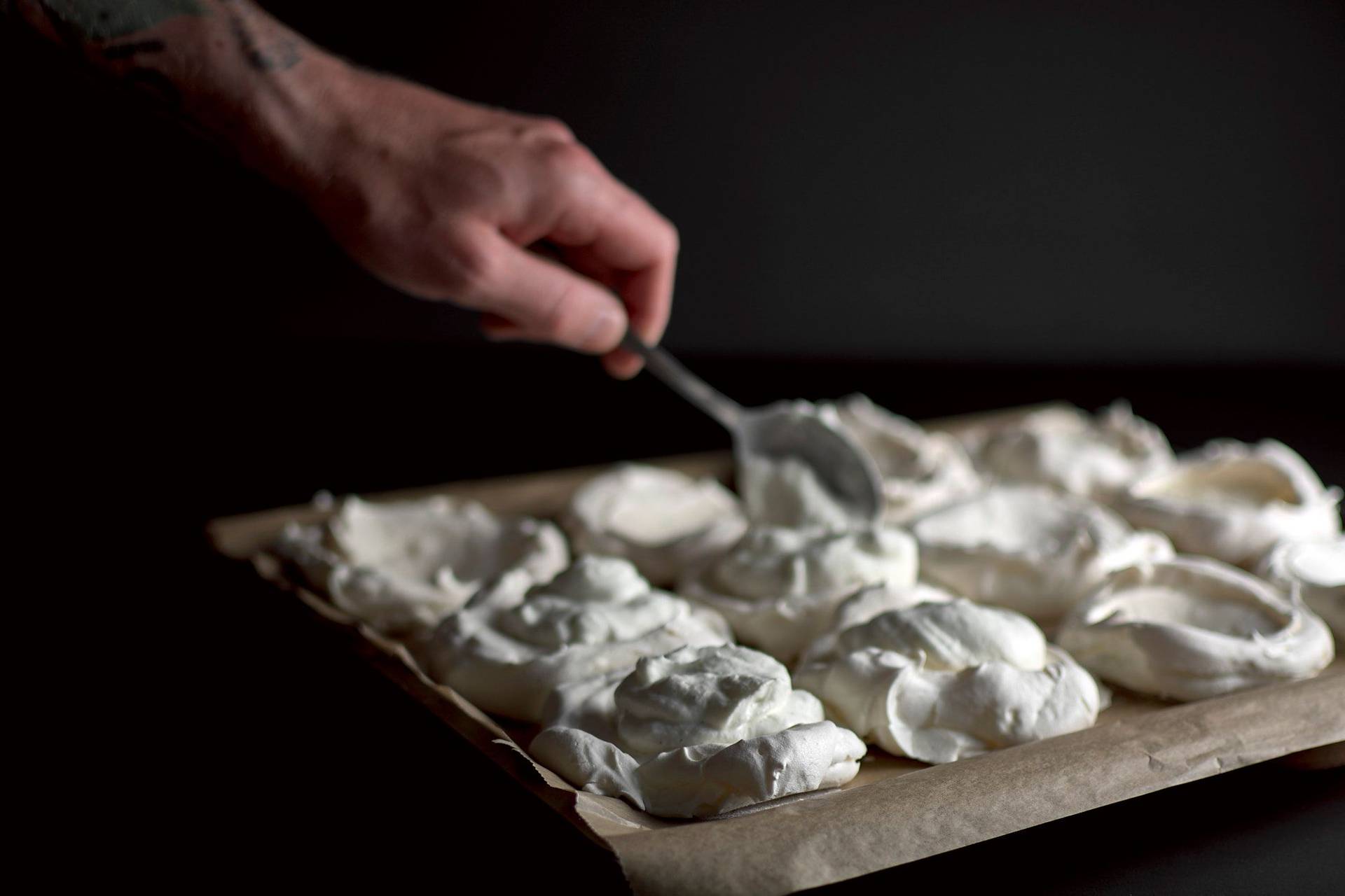 pavlova-fuellen pavlova wird auf einem backblech mit sahne gefüllt vor schwarzem hintergrund