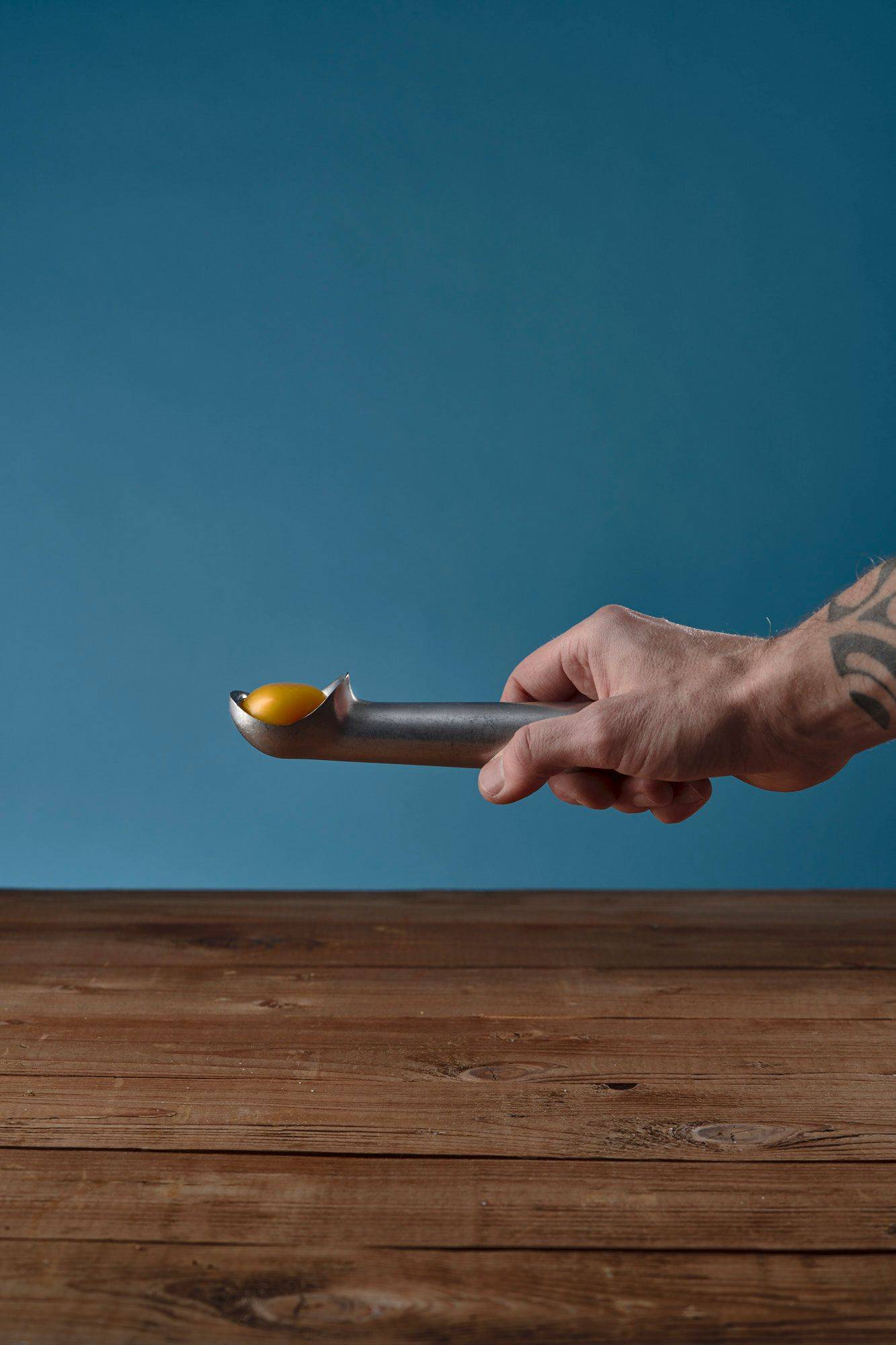 egg-yolk hand holding an ice cream spoon with egg yolk on a wooden table with blue background