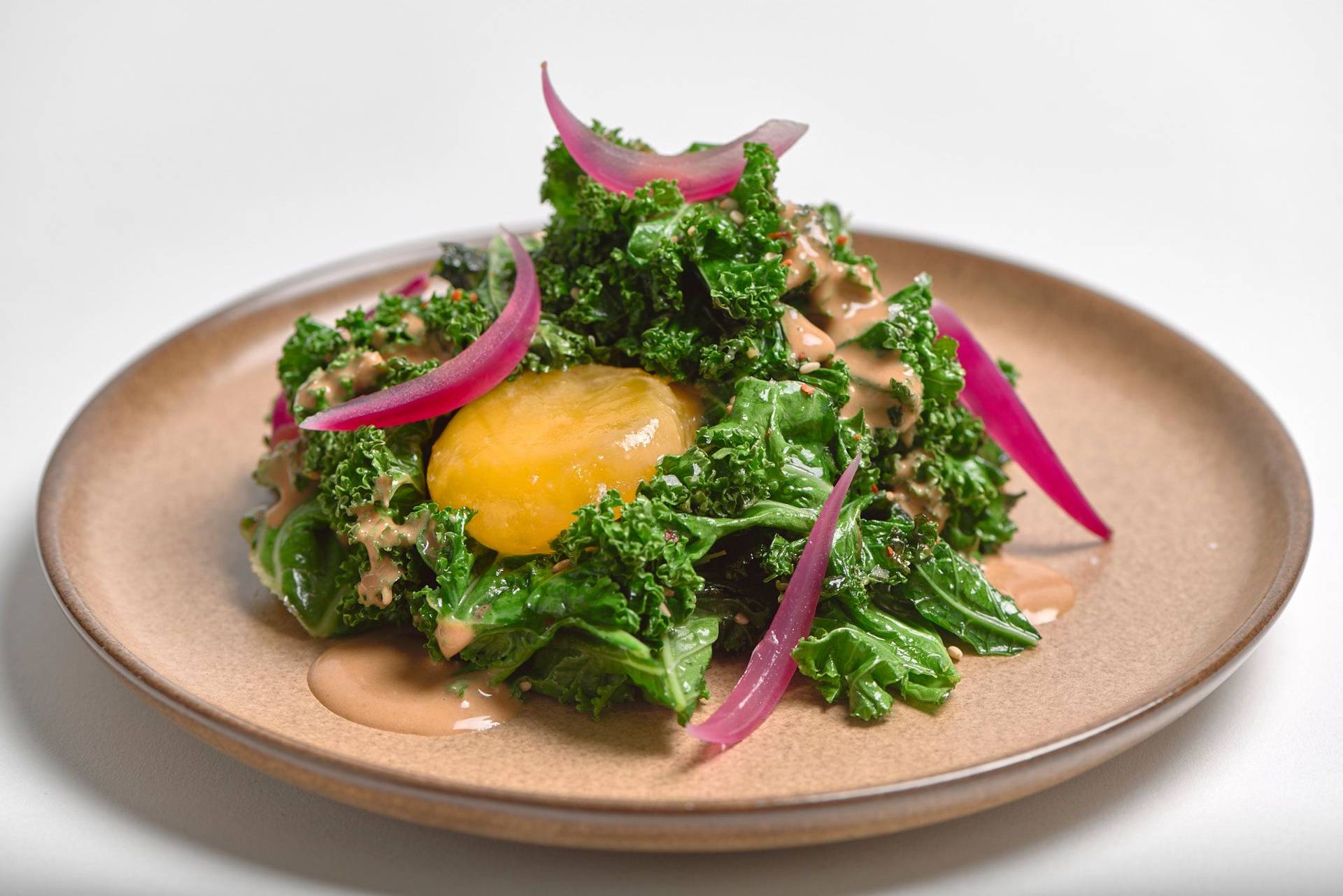 grünkohl salat mit miso eigelb und hagebutte auf einem braunen keramik teller mit weißem hintergrund