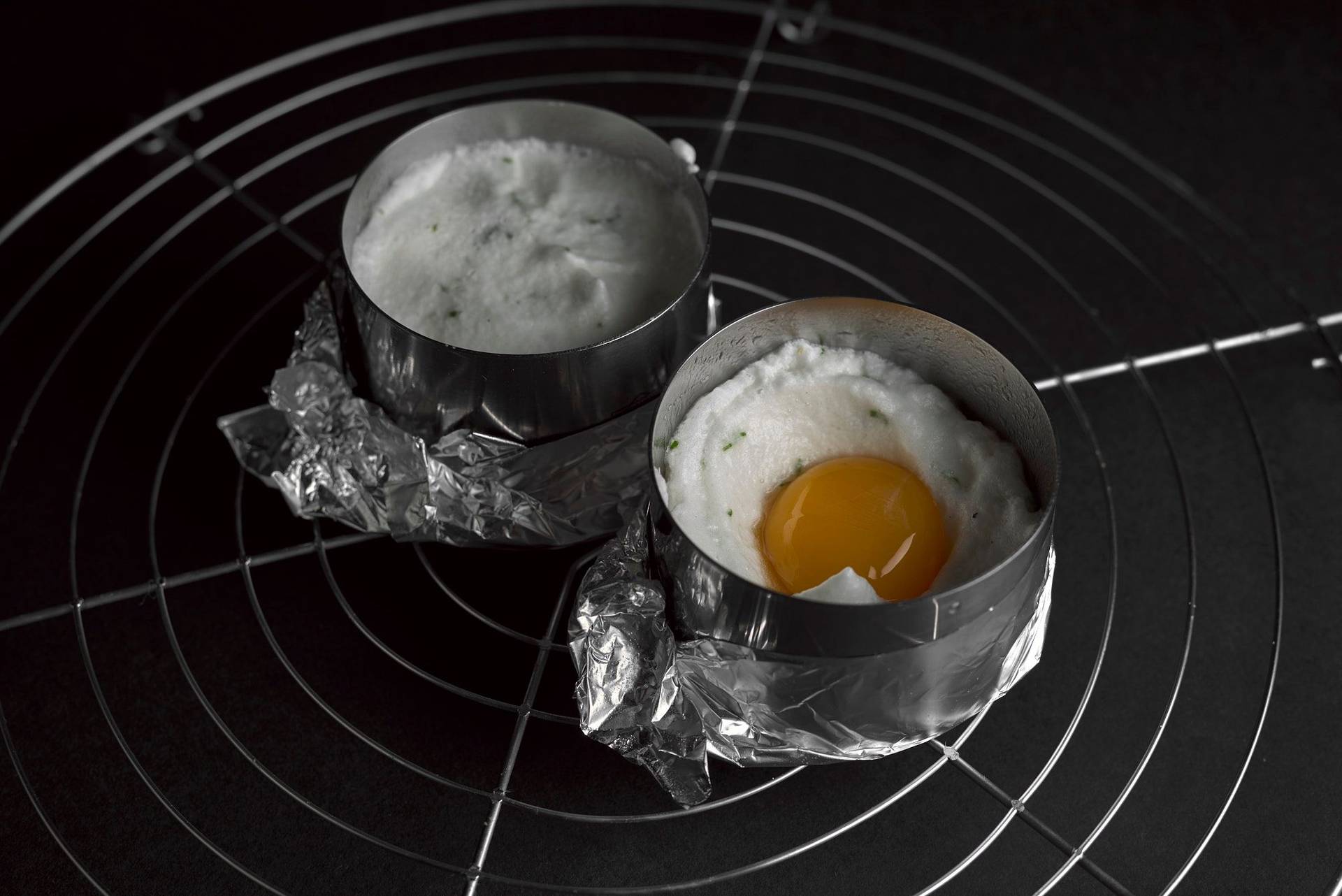 two raw egg soufflés on a baking grid on black background