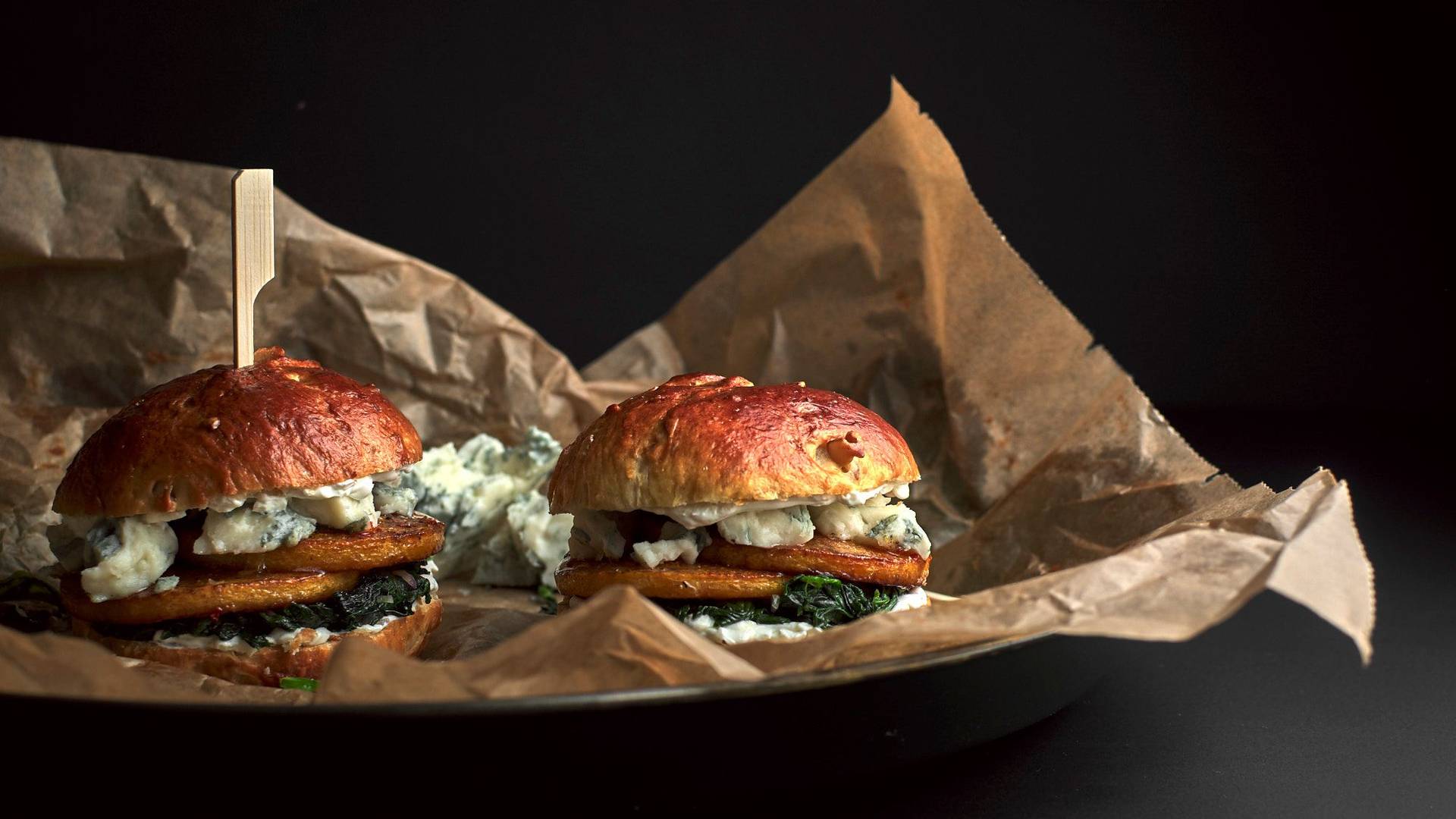 vegetarischer Kürbis-Brioche Burger mit Blauschimmel Käse und Spinat vor schwarzem Hintergrund