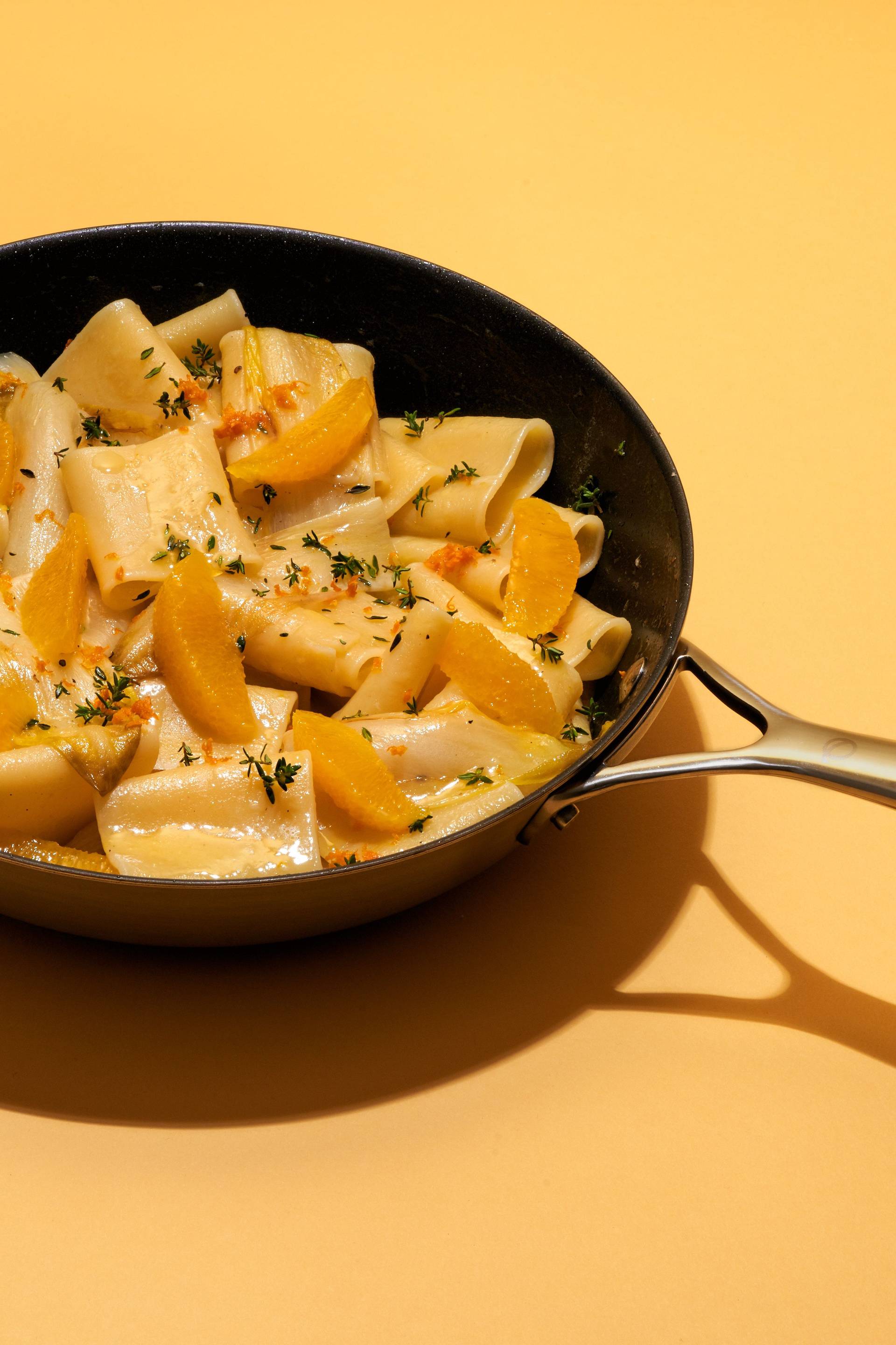 eine olav pfanne mit vegetarische one pot pasta mit chicoree und orange auf gelbem hintergrund auf gelbem hintergrund