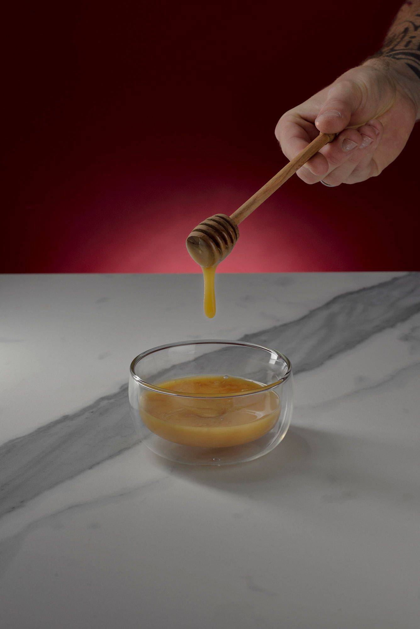 honey honey in a glass bowl on marbled sapienstone top with red background