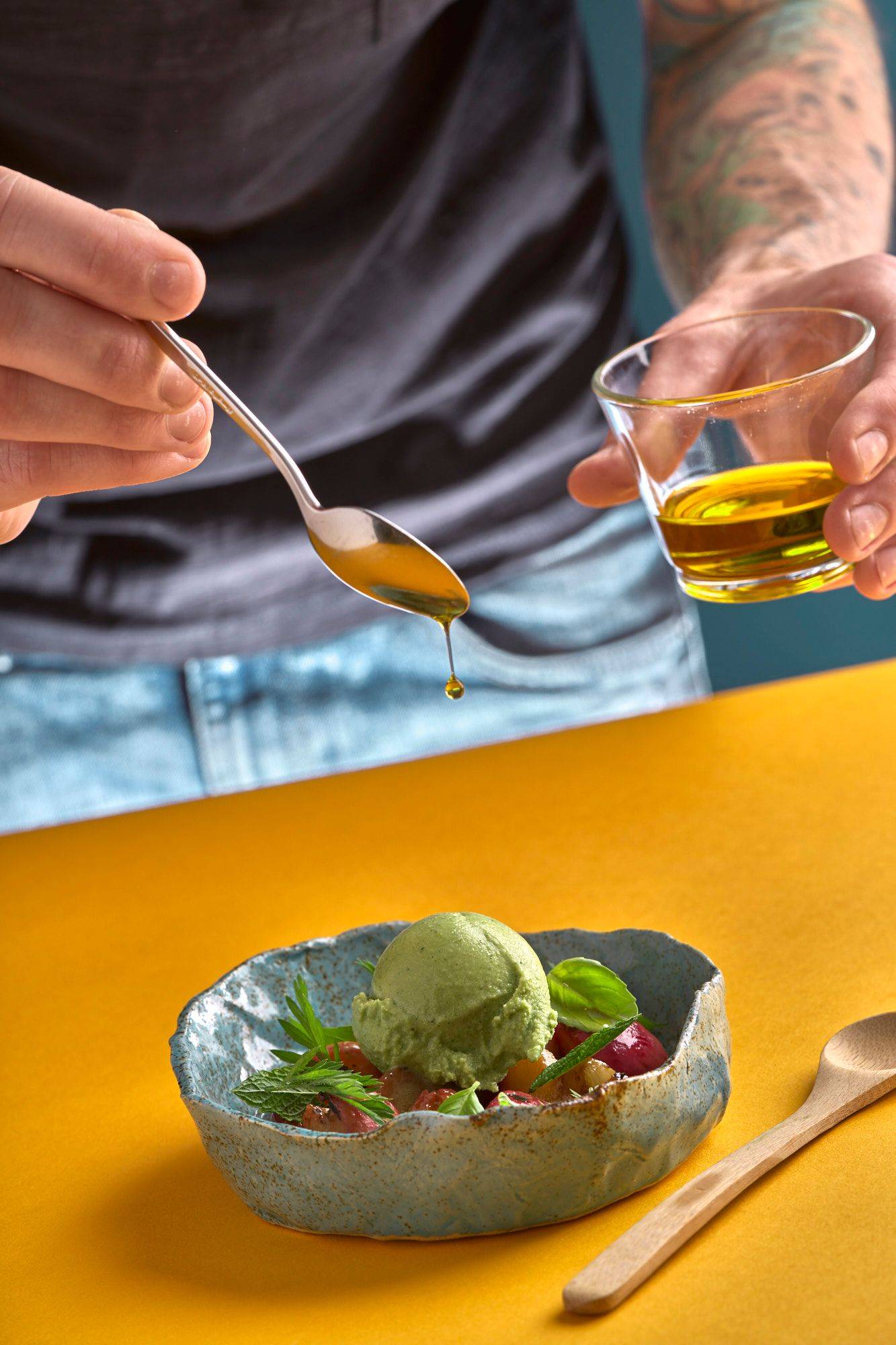 herbs and yogurt ice cream with grilled peaches and greek olive oil in a turquoise ceramic bowl with yellow and blue background